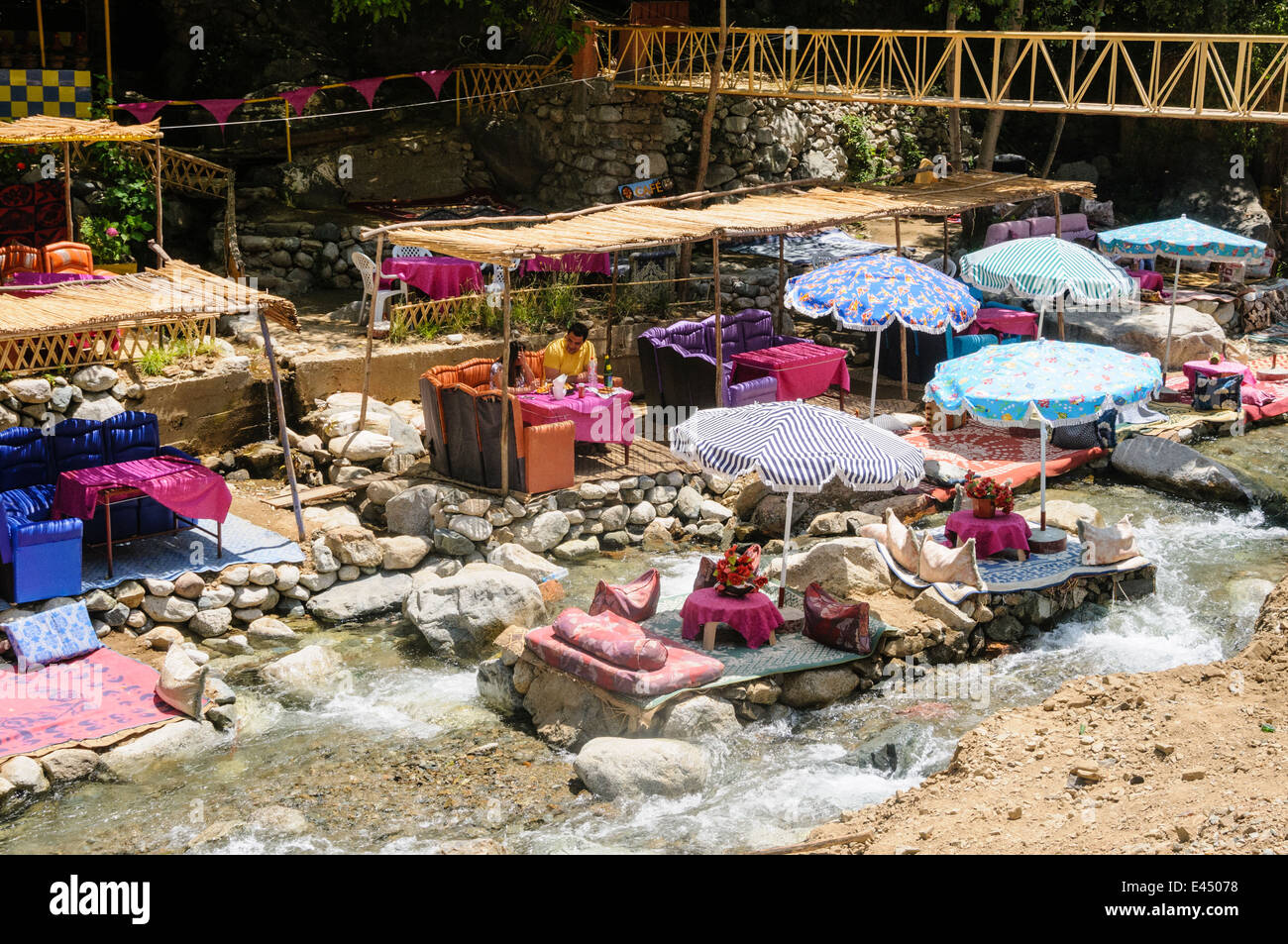 Tables, chaises de patio en plastique avec des parasols dans les restaurants sur les rives de la rivière de l'Ourika, la vallée de l'Ourika, Atlas, Maroc Banque D'Images