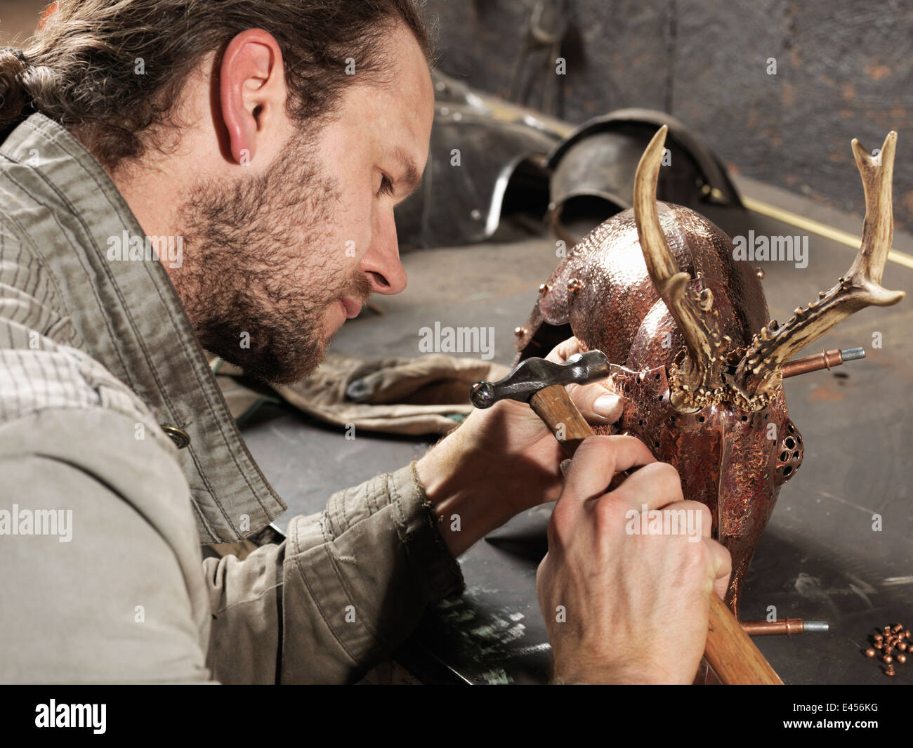 Marteau de forgeron sur cuivre sculpture de cerf en atelier Banque D'Images