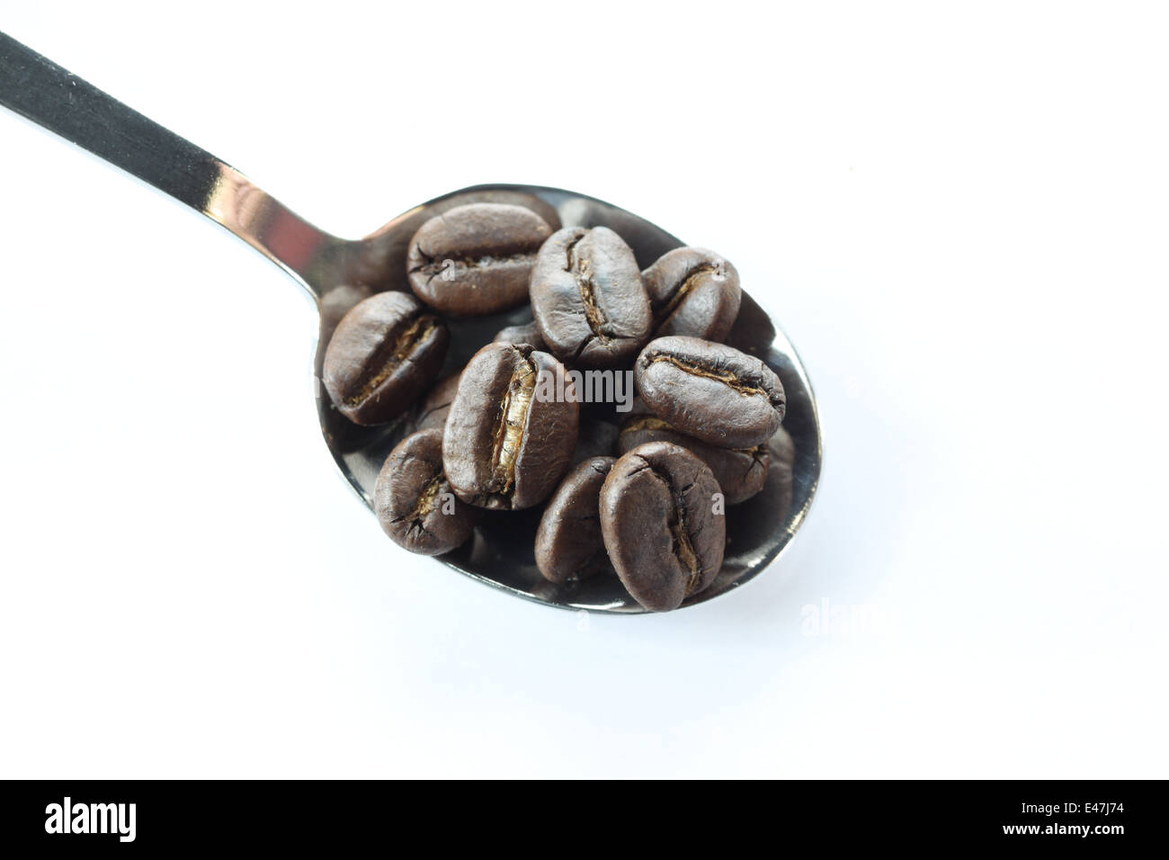 Grains de café dans une cuillère en acier inoxydable sur fond blanc. Banque D'Images