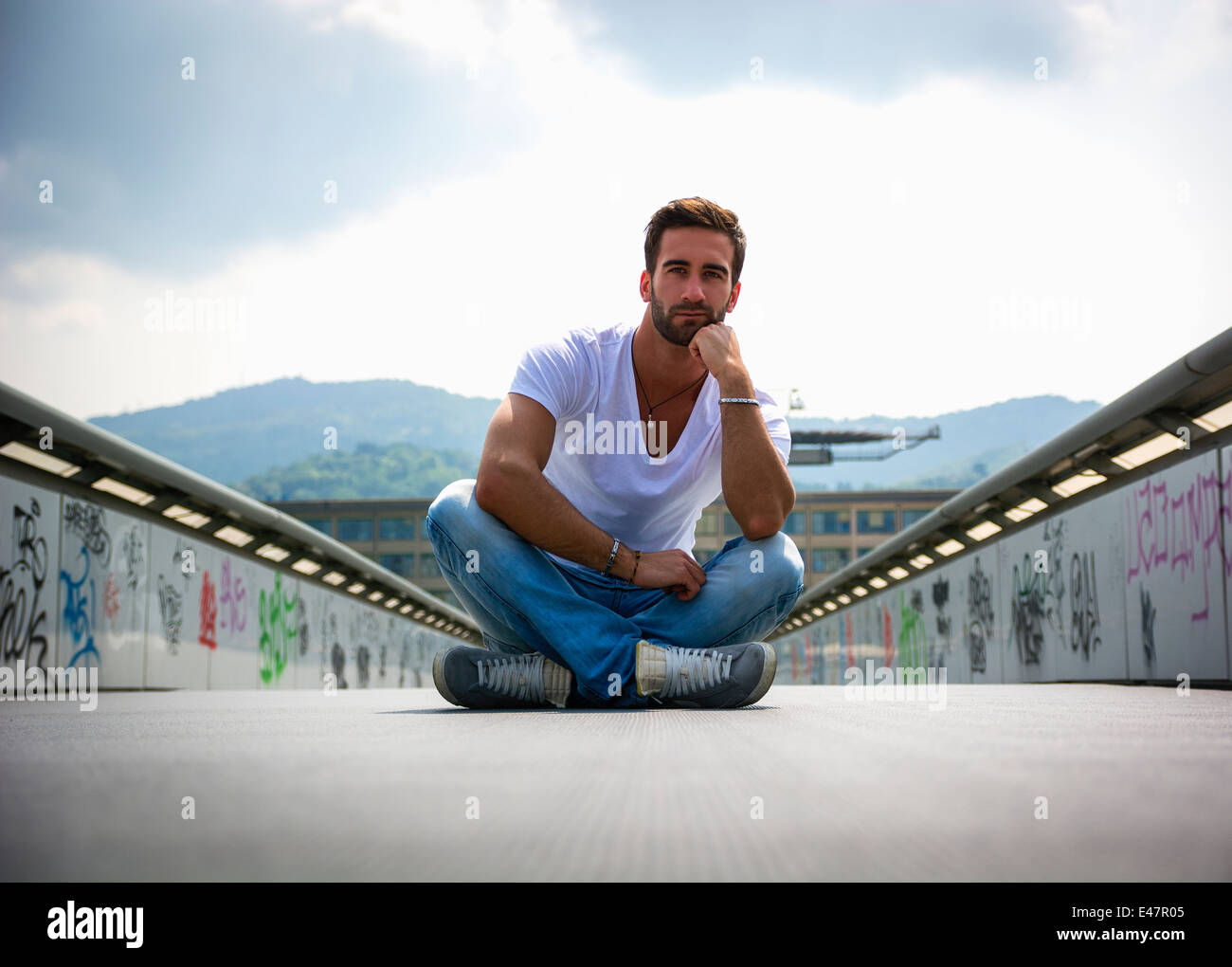 Beau jeune homme barbu assis à l'extérieur dans l'environnement urbain looking at camera Banque D'Images