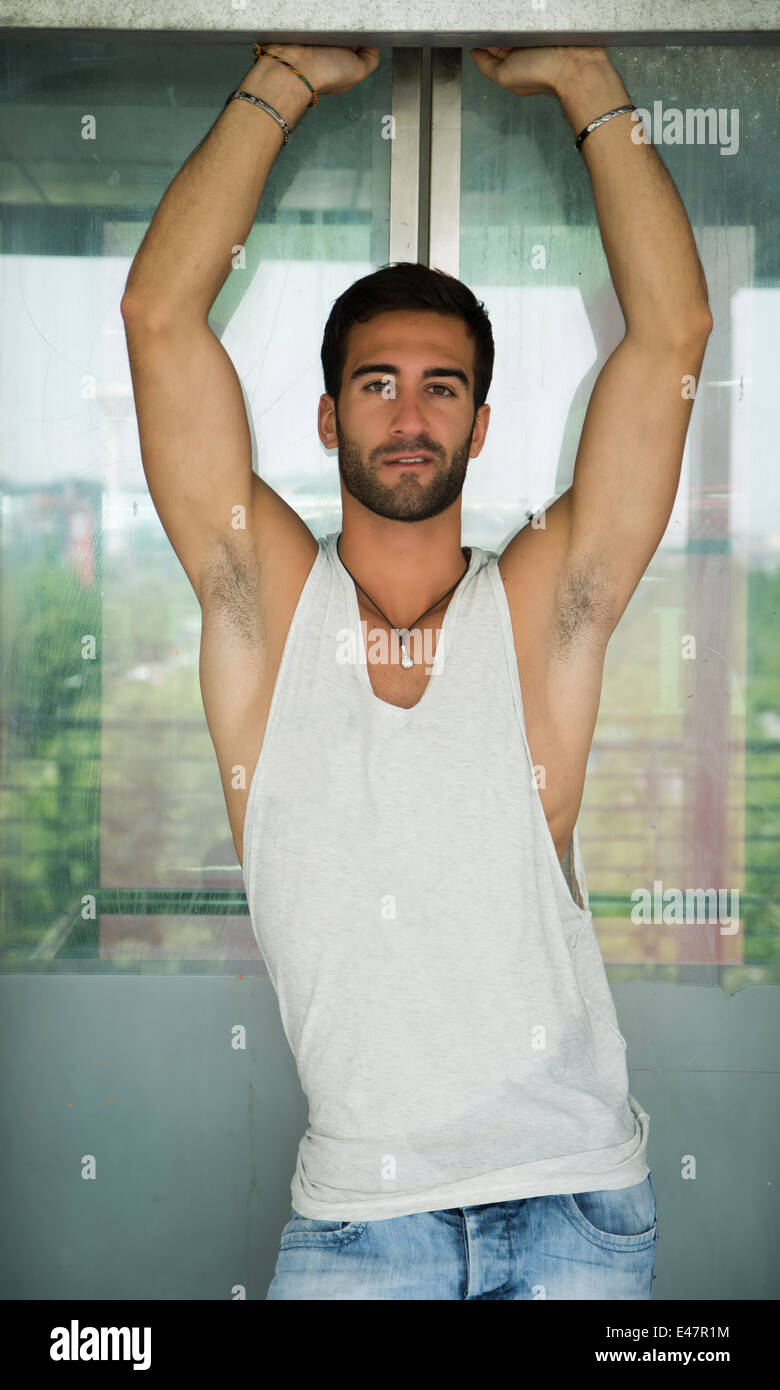 Beau jeune homme barbu à l'extérieur dans l'environnement urbain, avec les bras au-dessus de la tête Banque D'Images