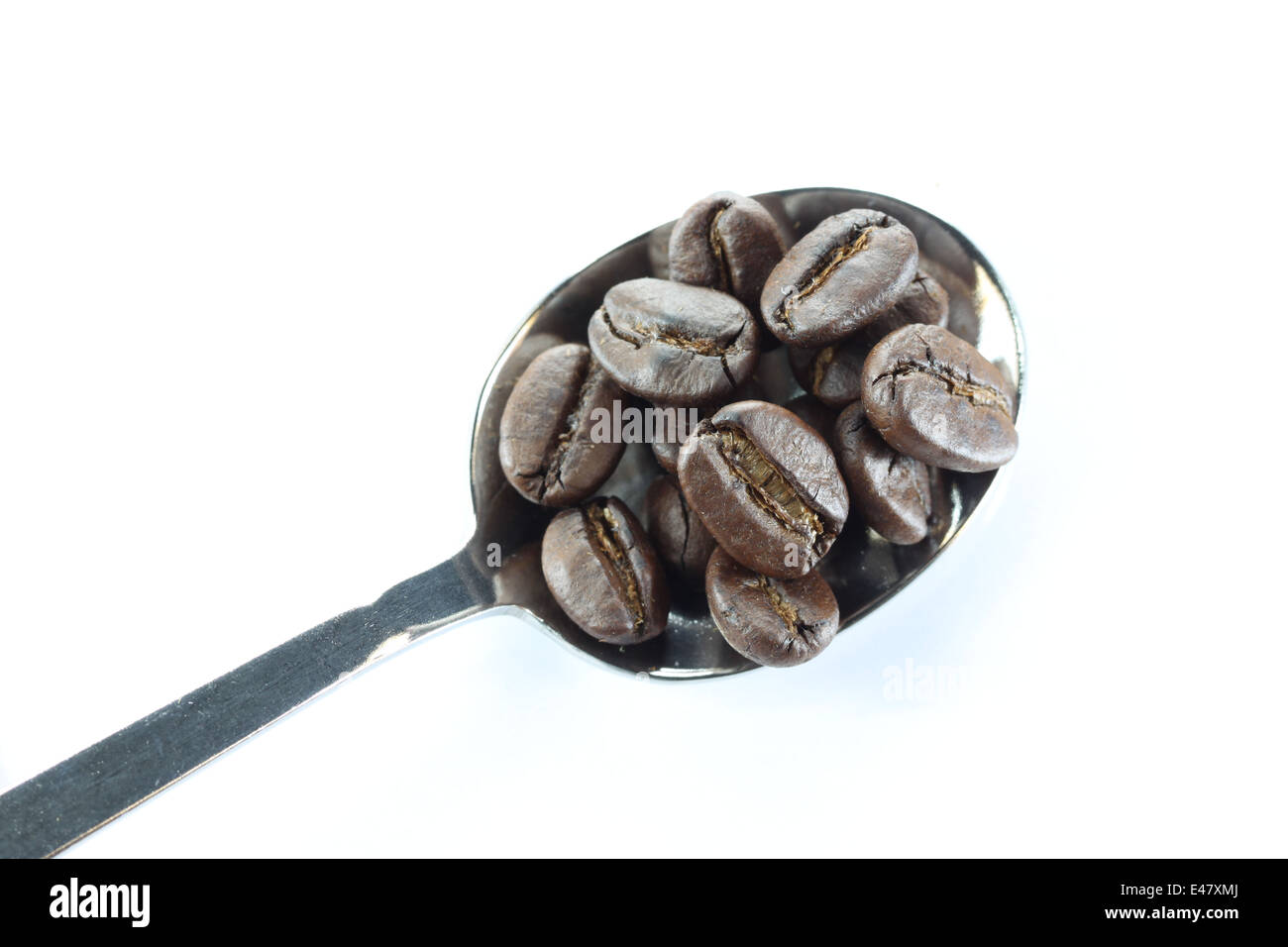 Grains de café dans une cuillère en acier inoxydable sur fond blanc. Banque D'Images