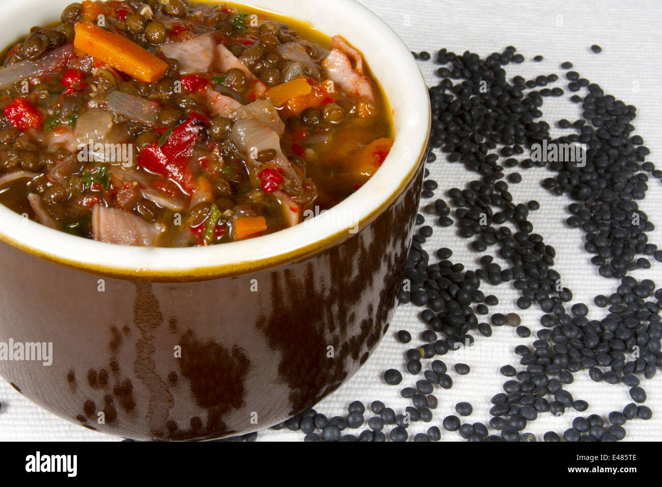 Bol de soupe faite avec les lentilles beluga, carottes, poivrons et jambon sur le linge blanc Banque D'Images