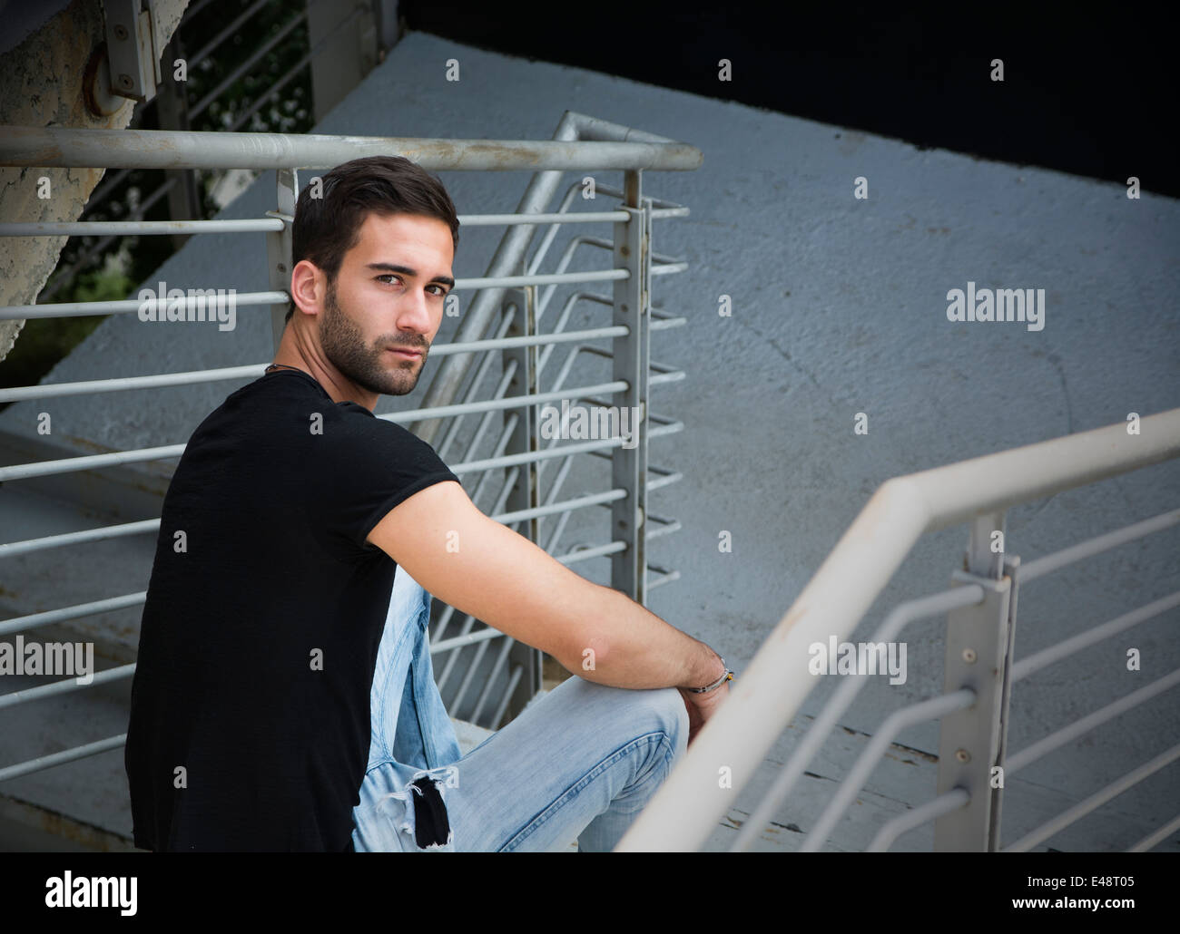 Beau jeune homme barbu assis à l'extérieur dans l'environnement urbain looking at camera Banque D'Images