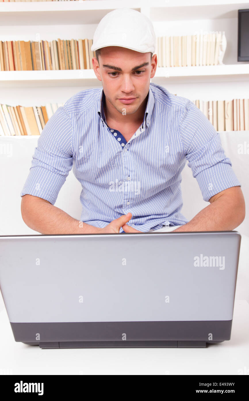 Mode jeune homme portant un chapeau et chemise à la recherche à l'écran de l'ordinateur en face d'étagère Banque D'Images