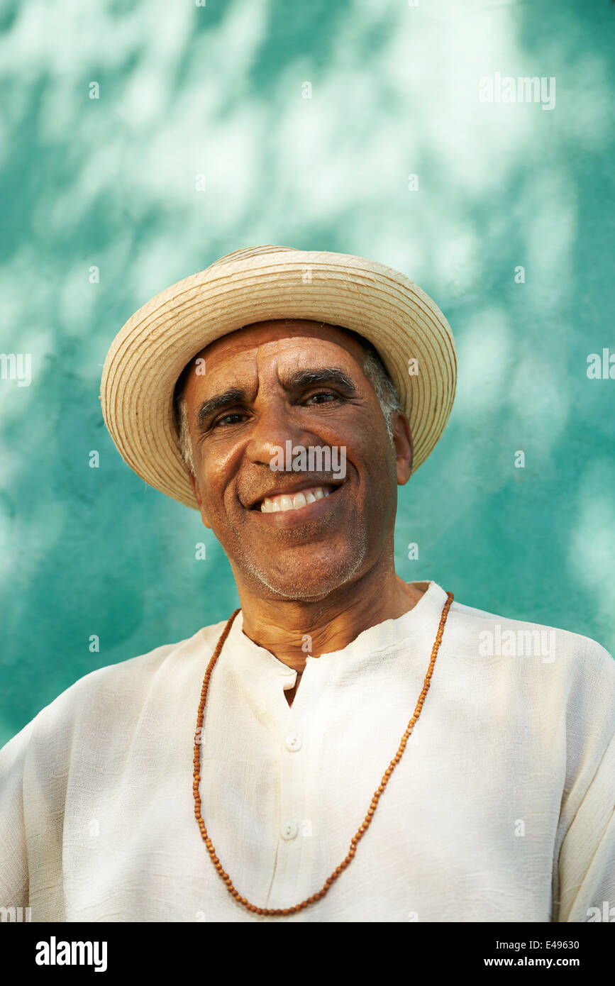 Portrait de senior retraité hispanic man with straw hat assis dans un parc et à la recherche à l'appareil photo avec l'expression heureuse Banque D'Images