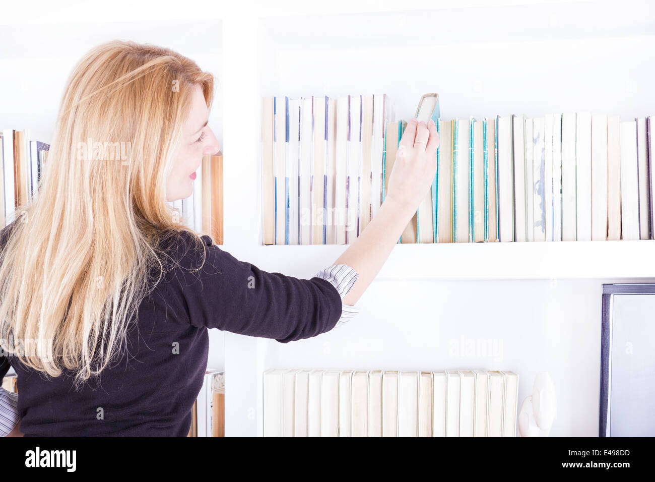 Femme blonde en tirant un livre de bibliothèque, étagère off girl selecting book from bookshelf Banque D'Images