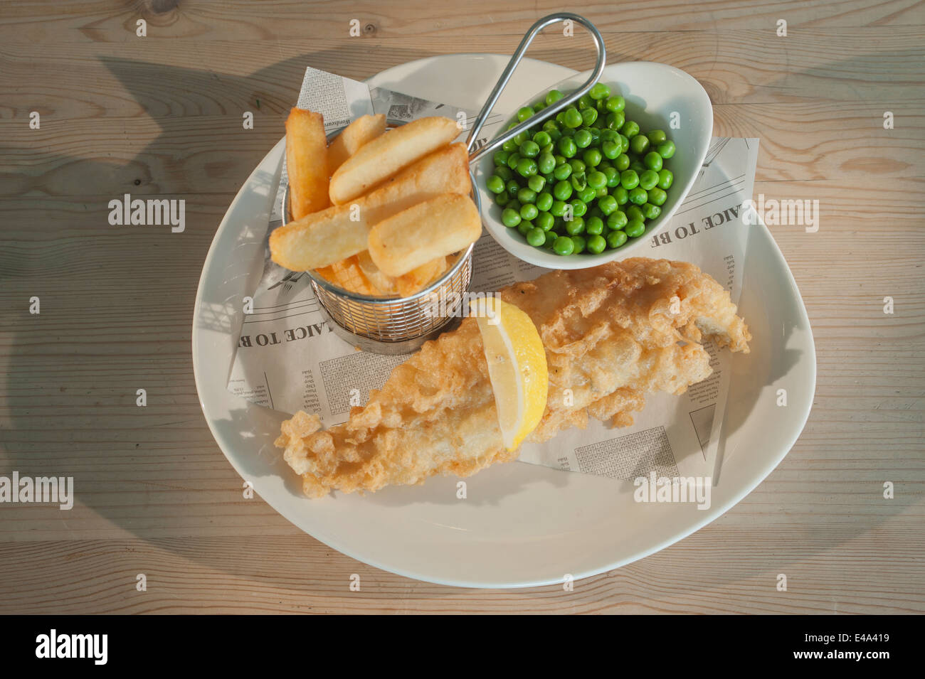 Fish and chips (l'aiglefin en pâte) avec des petits pois et un segment de citron sur une plaque blanche sur une table en bois. Banque D'Images