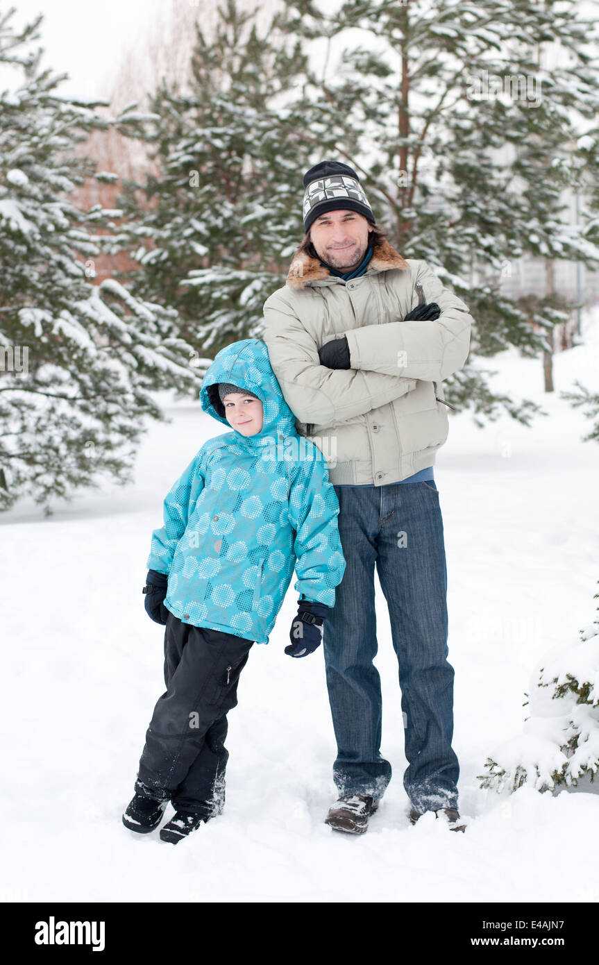 Famille son père, père de l'enfant de la neige deux vacances d'hiver forêt du parc à pied se trouvent des arbres Pin epicéa vêtements hat cap jacket light blue Banque D'Images
