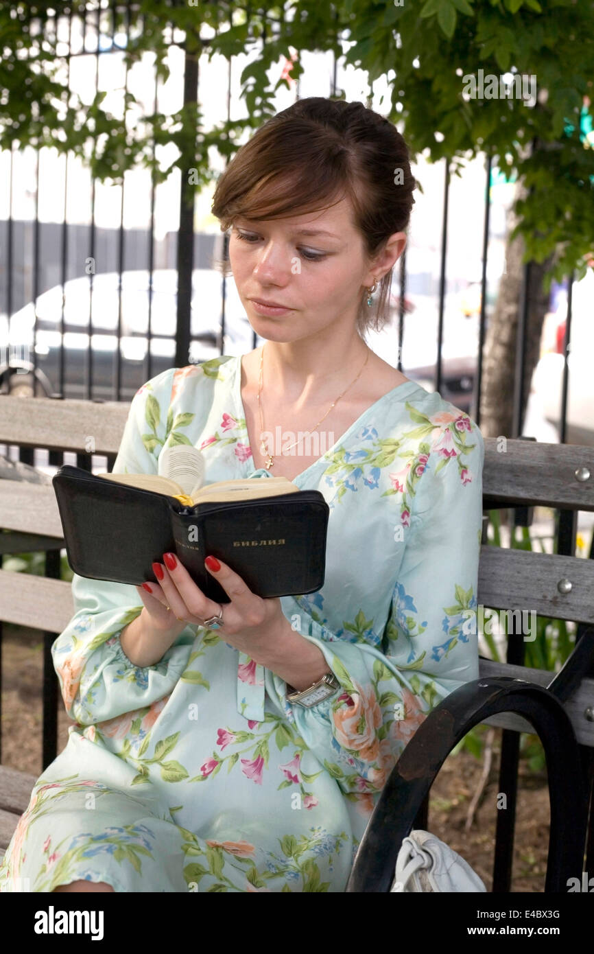 Jeune fille russe se trouve dans le parc et lit sa Bible russe. Elle se trouvait dans sa fin des années 20 au moment de tirer. Banque D'Images