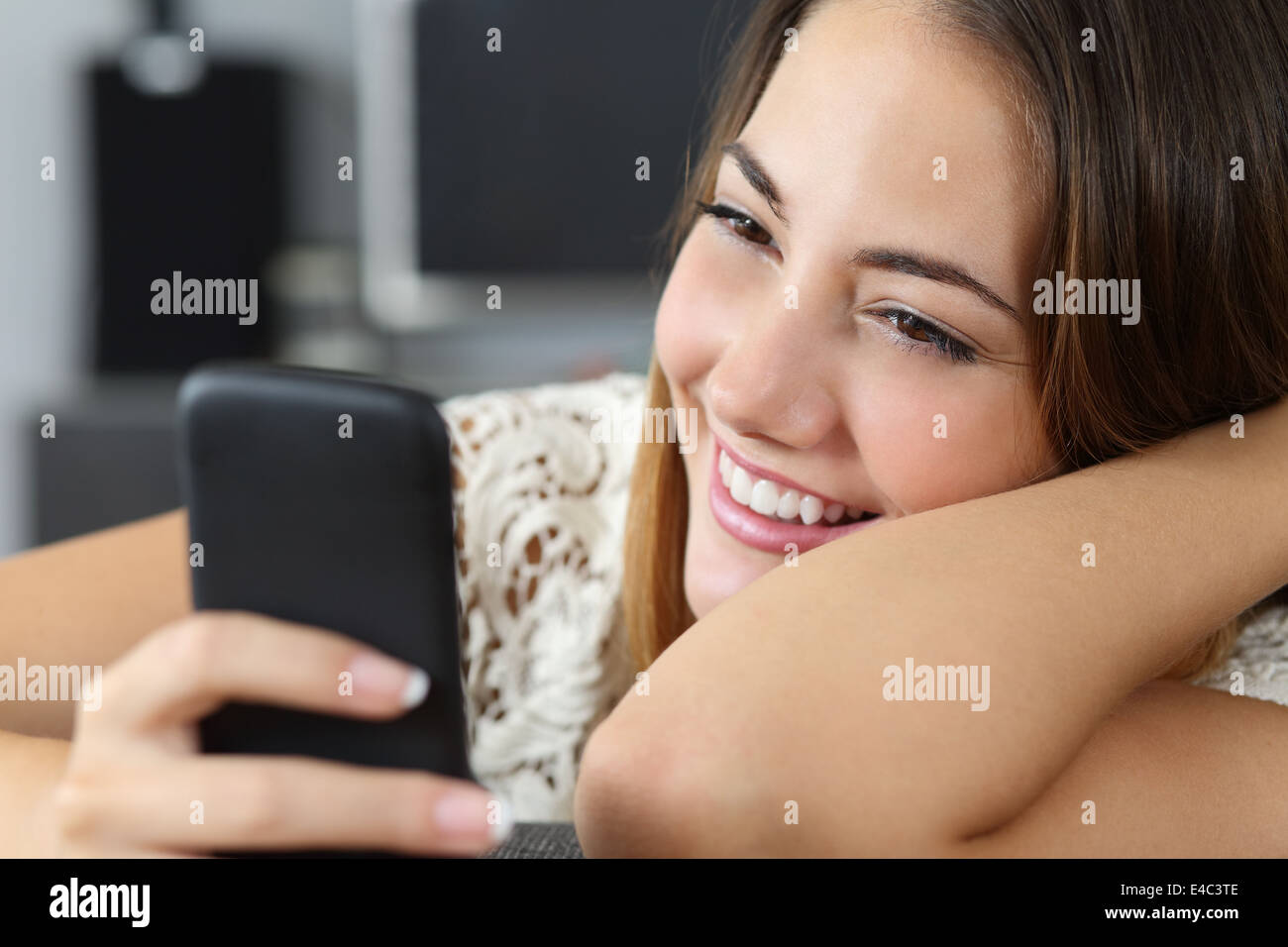 Femme drôle en utilisant un téléphone intelligent à la maison sur un sofa texting and smiling Banque D'Images