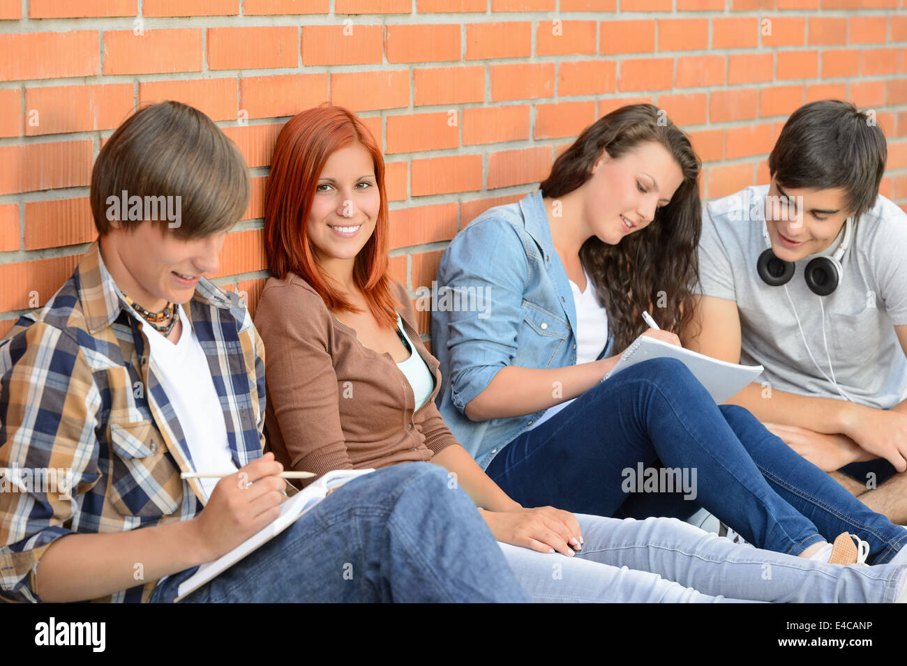 College students sitting in row against brick wall writing notes Banque D'Images