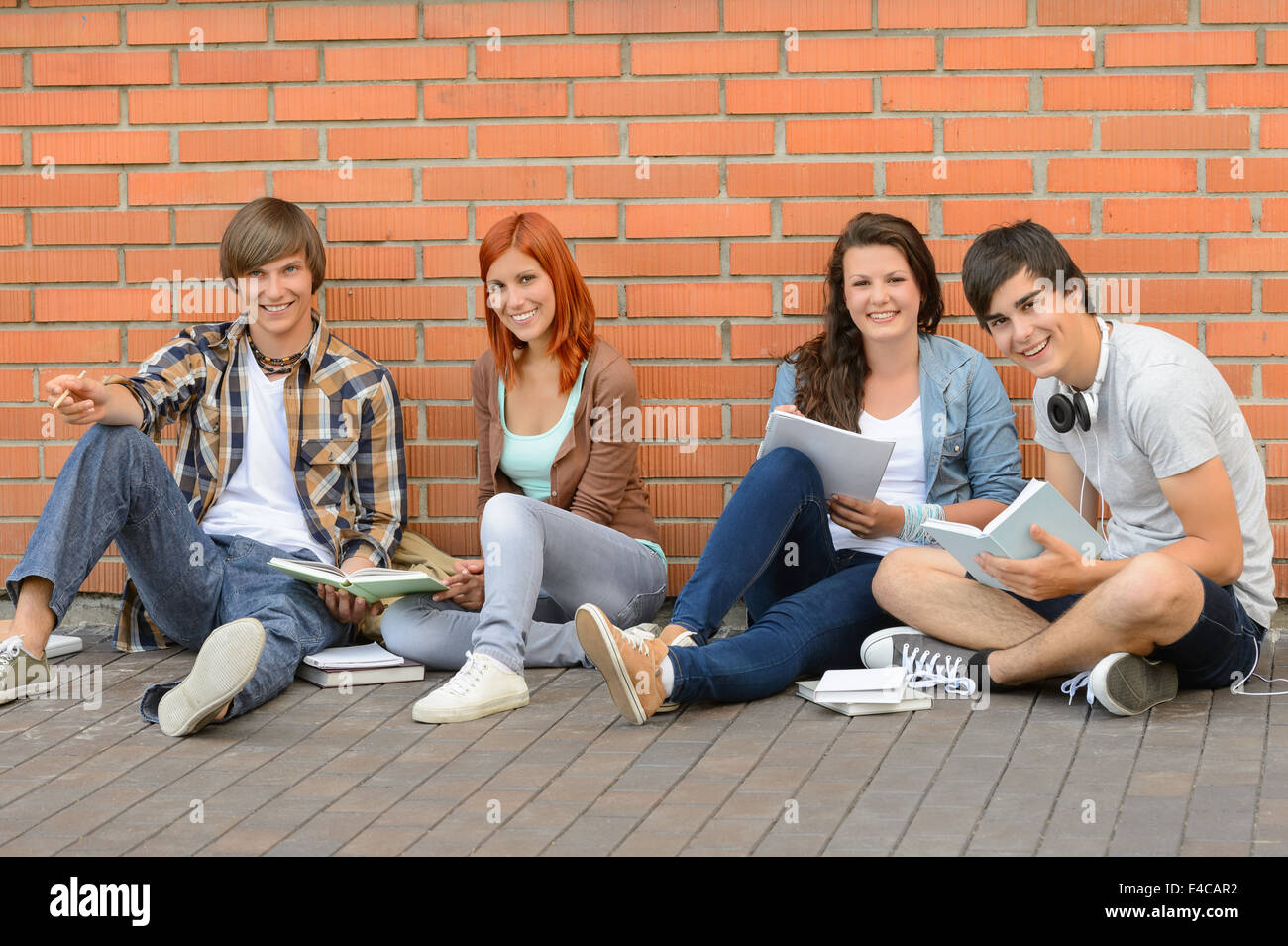 Les élèves du collège avec des livres assis par terre brick wall Banque D'Images