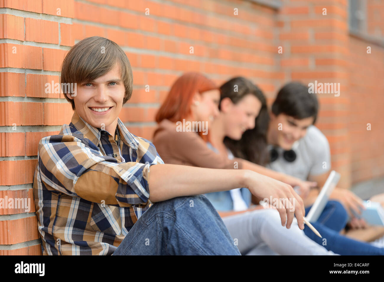 Élève garçon assis par brick wall friends smiling in background Banque D'Images