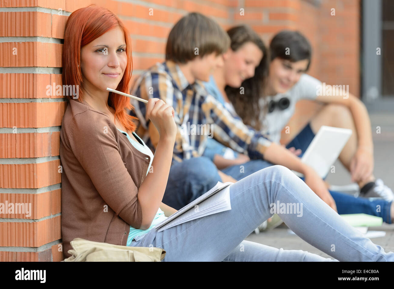 L'étude de jeune femme avec des amis assis sur le sol à l'extérieur de college Banque D'Images