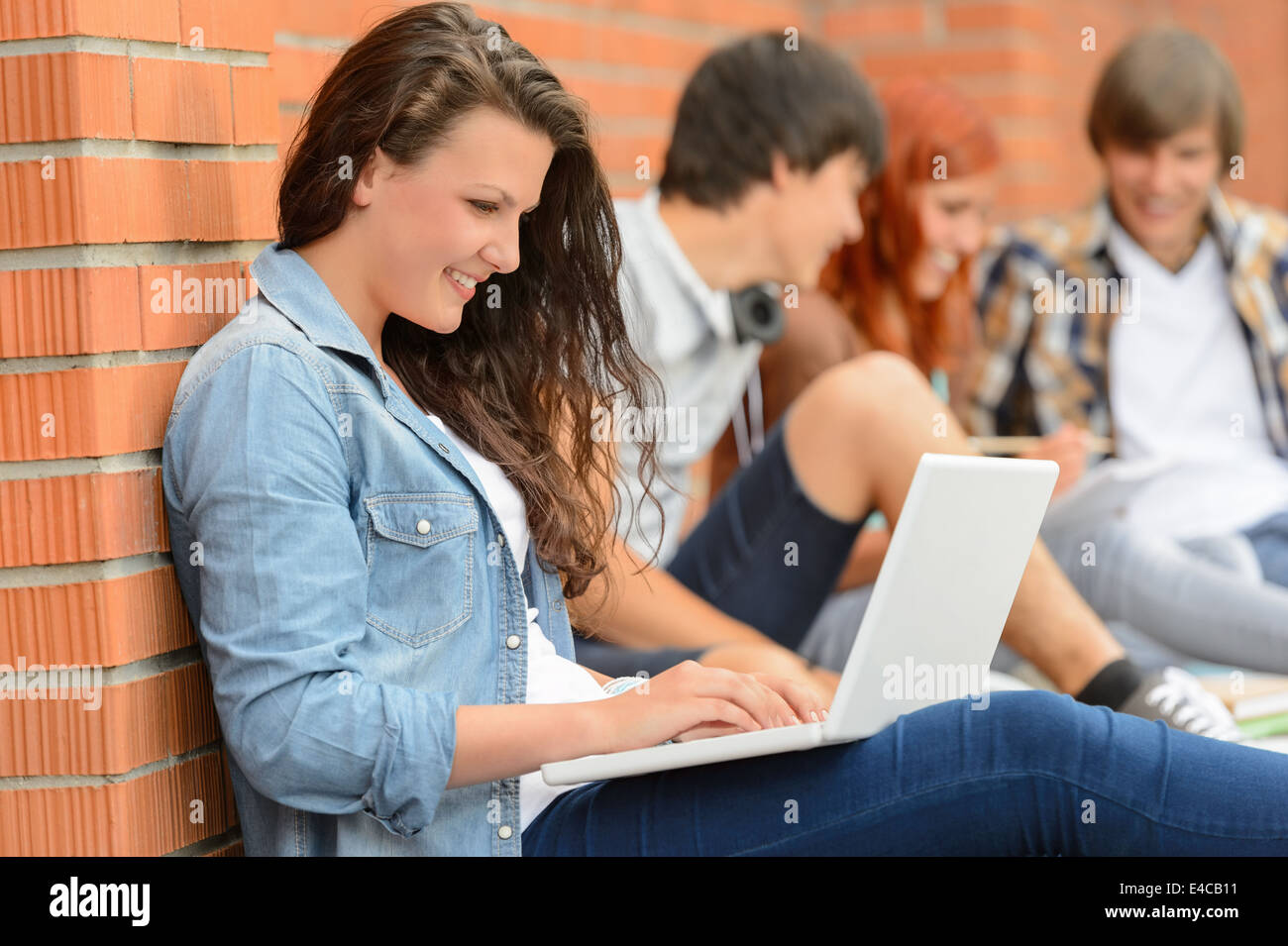 Student girl working on laptop hors college friends en arrière-plan Banque D'Images
