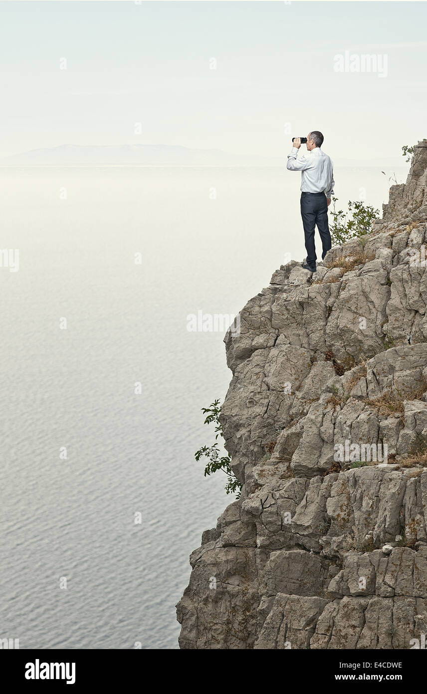 Homme debout sur la falaise à la recherche avec des jumelles Banque D'Images
