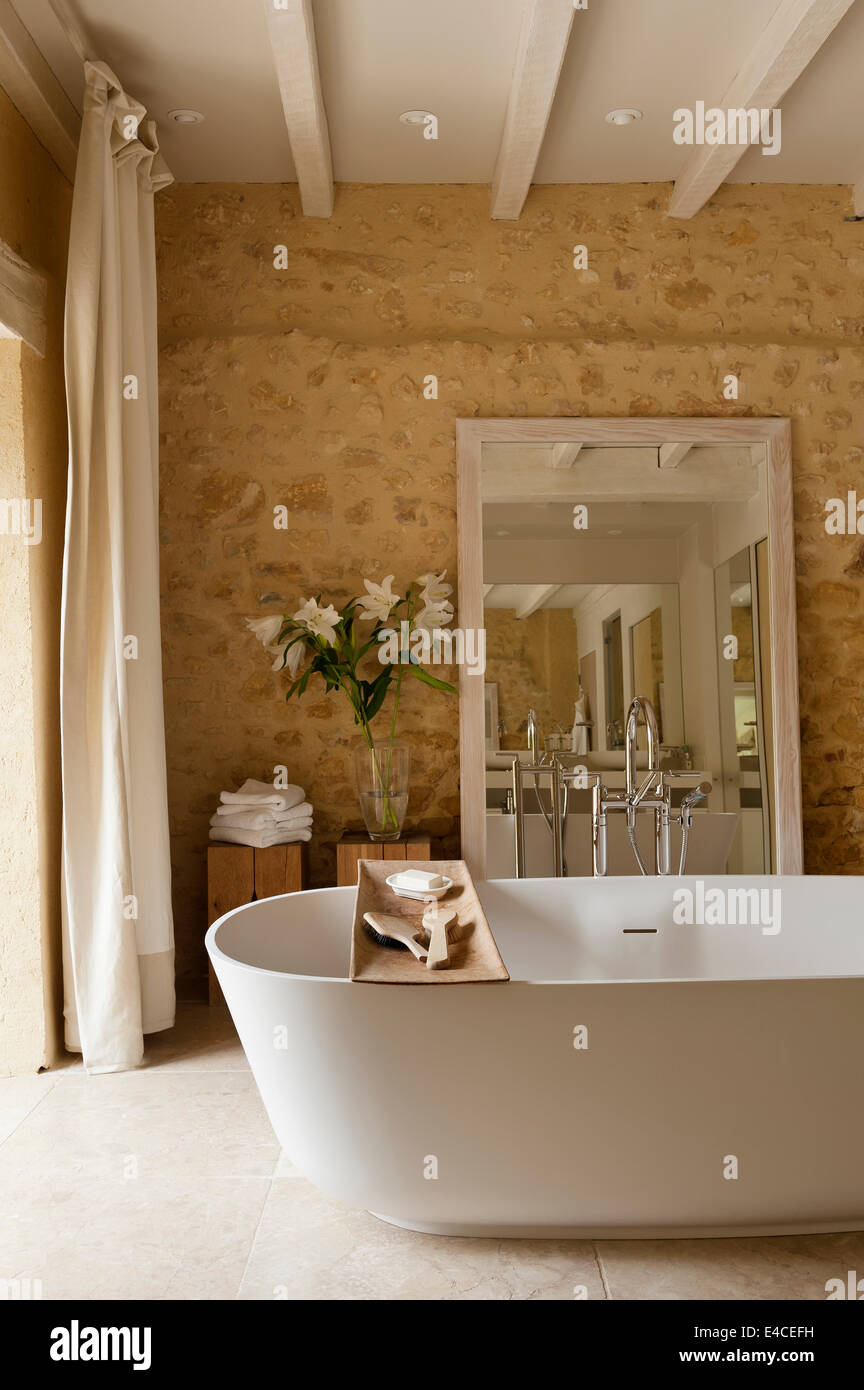 Une profonde baignoire 910 AV de l'agapè dans la salle de bains avec des murs en pierre et un grand miroir Banque D'Images