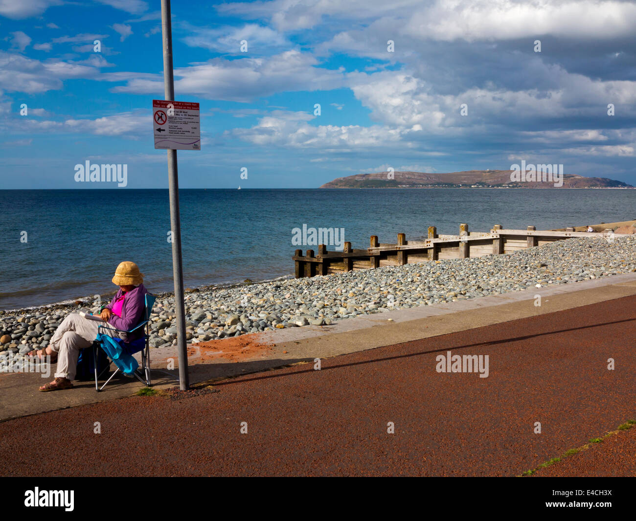 Woman relaxing on deck chair sur la plage à Penmaenmawr Conwy dans le Nord du Pays de Galles UK avec le Great Orme et distance dans Llandudno Banque D'Images