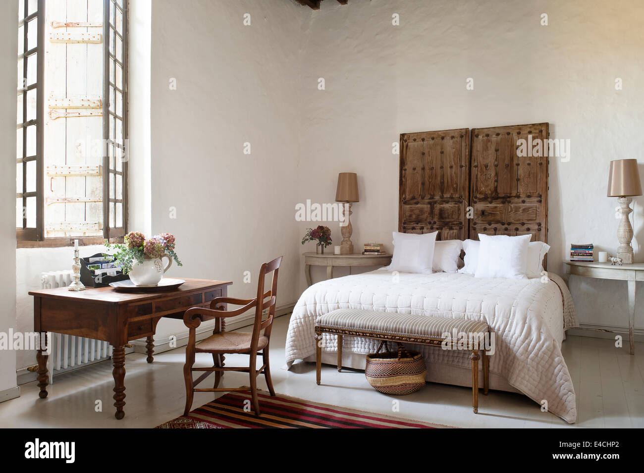 Ancienne paire de portes cloutées derrière lit dans la grande chambre blanche avec un bureau en bois Banque D'Images
