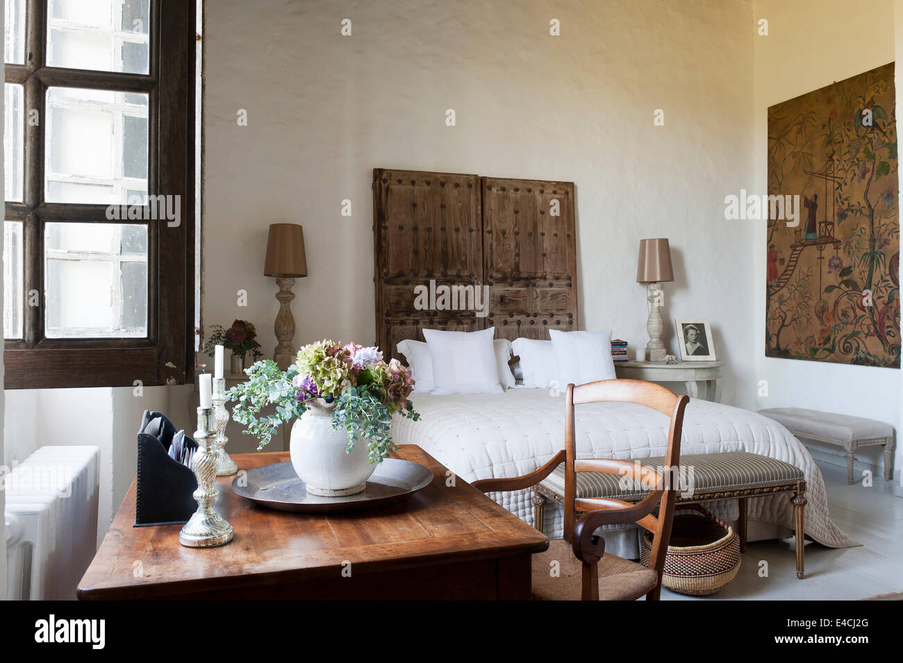 Ancienne paire de portes cloutées derrière lit dans la grande chambre blanche avec un bureau et de grandes œuvres Banque D'Images