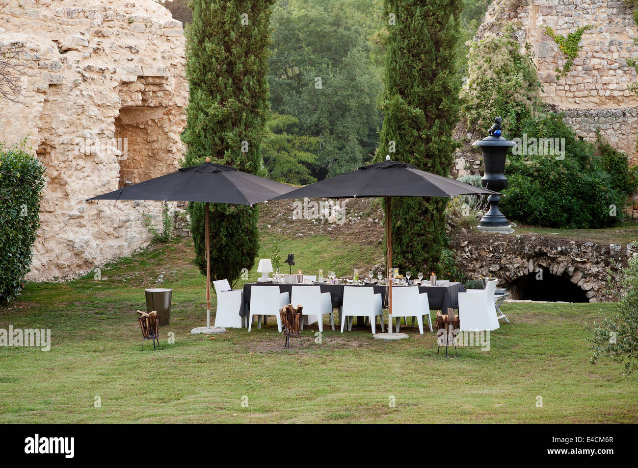 Un set de table pour le dîner sous une paire de parasols noir avec 11e siècle ruines et de cyprès en arrière-plan. La salle chai Banque D'Images