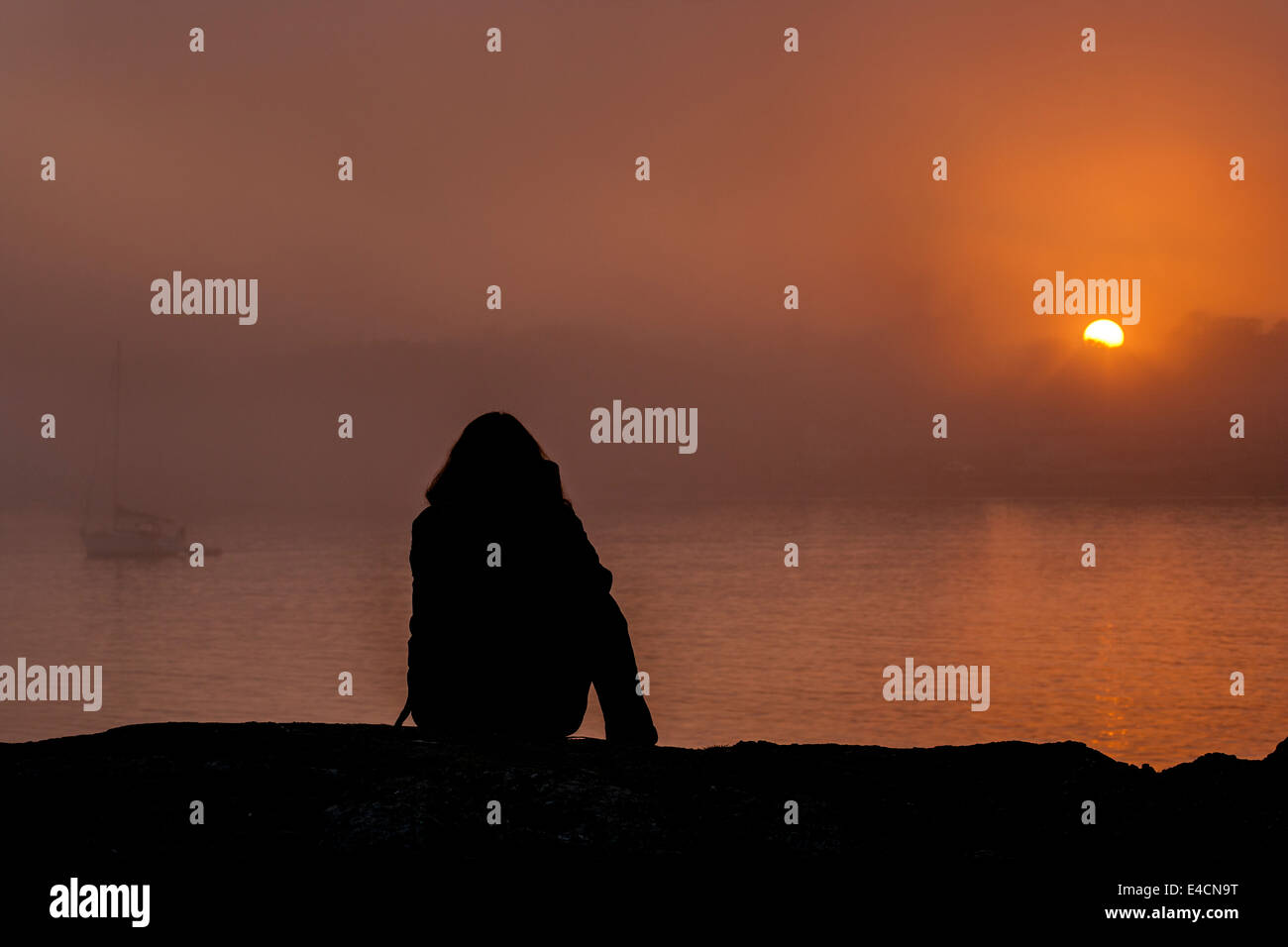 Woman relaxing et regarder le coucher du soleil à Point-Victoria misty Bovins, British Columbia, Canada. Banque D'Images