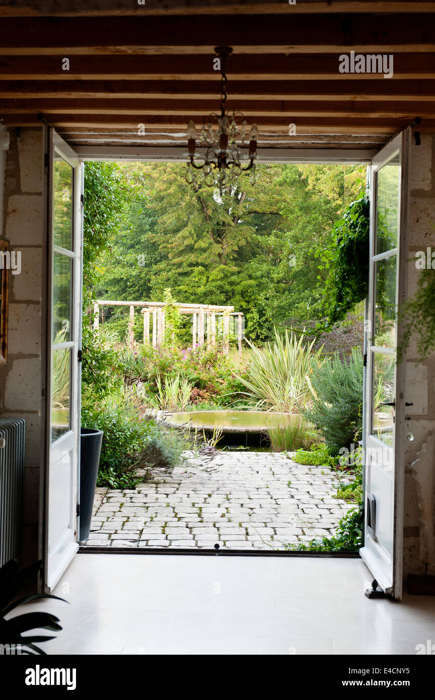 Voir à travers les portes-fenêtres donnant sur terrasse pavée et jardin luxuriant au-delà Banque D'Images
