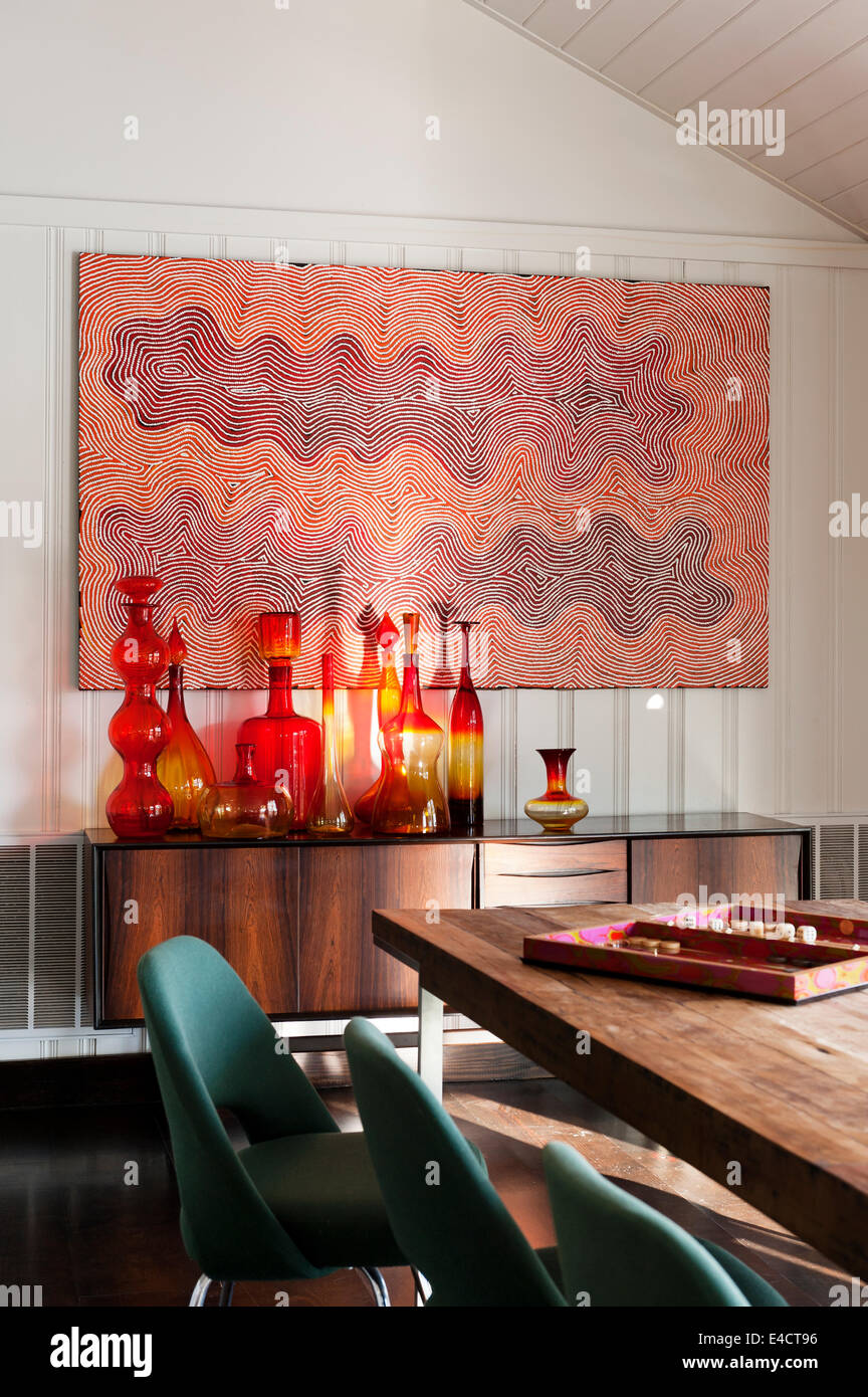 Une collection de verre Blenko américaine se dresse sur un bois de rose 1950 bahut. La peinture sur le mur est par un Australien Peuples autochtones Banque D'Images