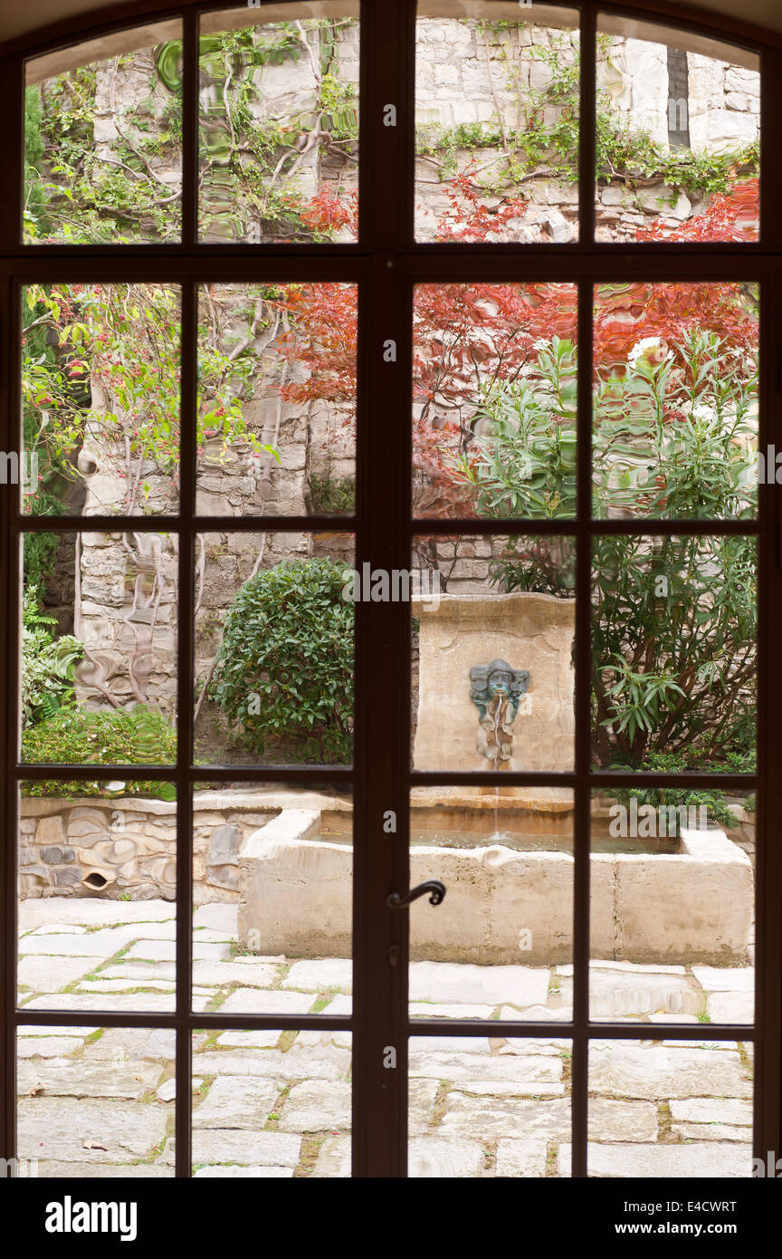 Vue à travers la porte en verre hors de cour avec fontaine en pierre Banque D'Images