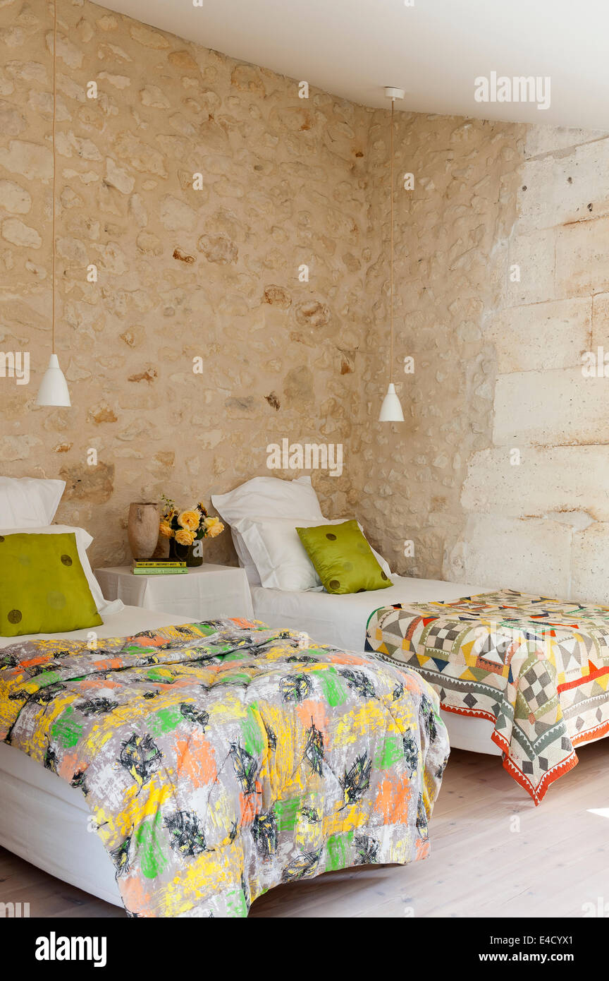 Chambre Lits Jumeaux avec lumières pendentif contemporain, vintage quilts et mur de pierres rugueuses Banque D'Images