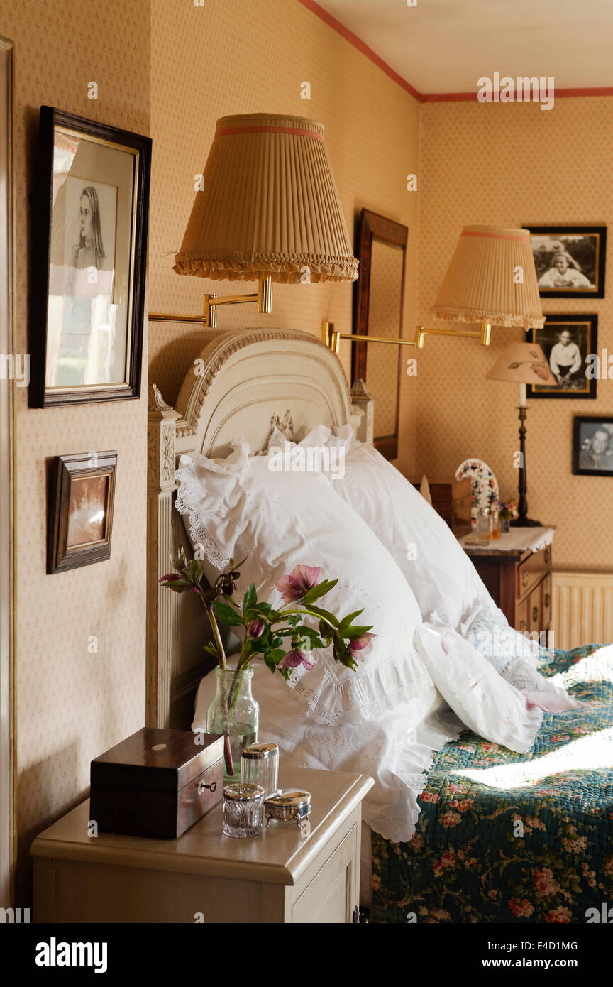 Gros coussins blancs sur un lit ancien avec détail sculpté dans une chambre avec du papier peint à motifs et des tables de chevet Banque D'Images