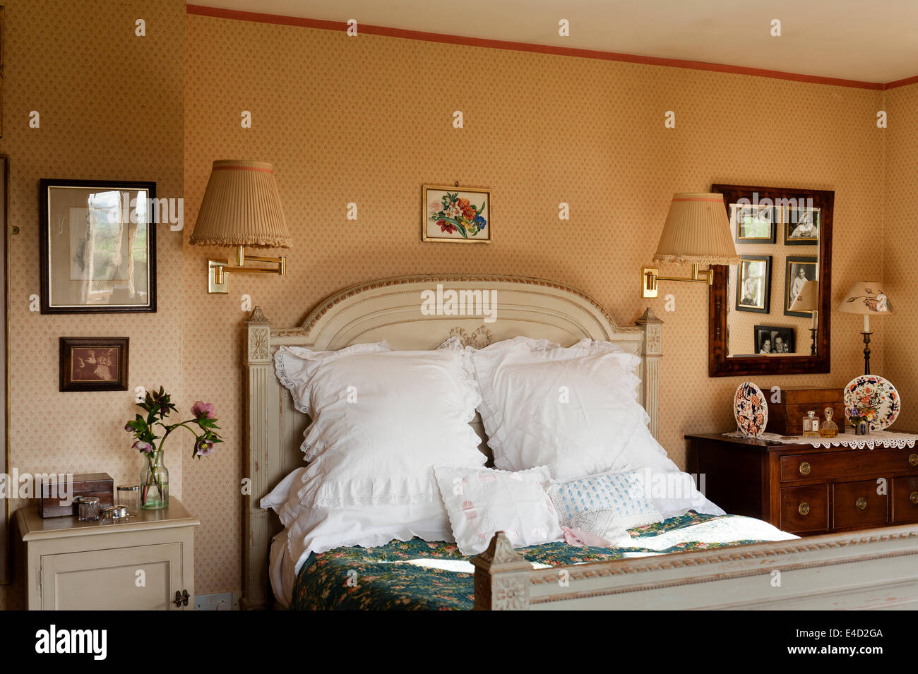 Gros coussins blancs sur un lit ancien avec détail sculpté dans une chambre avec du papier peint à motifs et des tables de chevet Banque D'Images