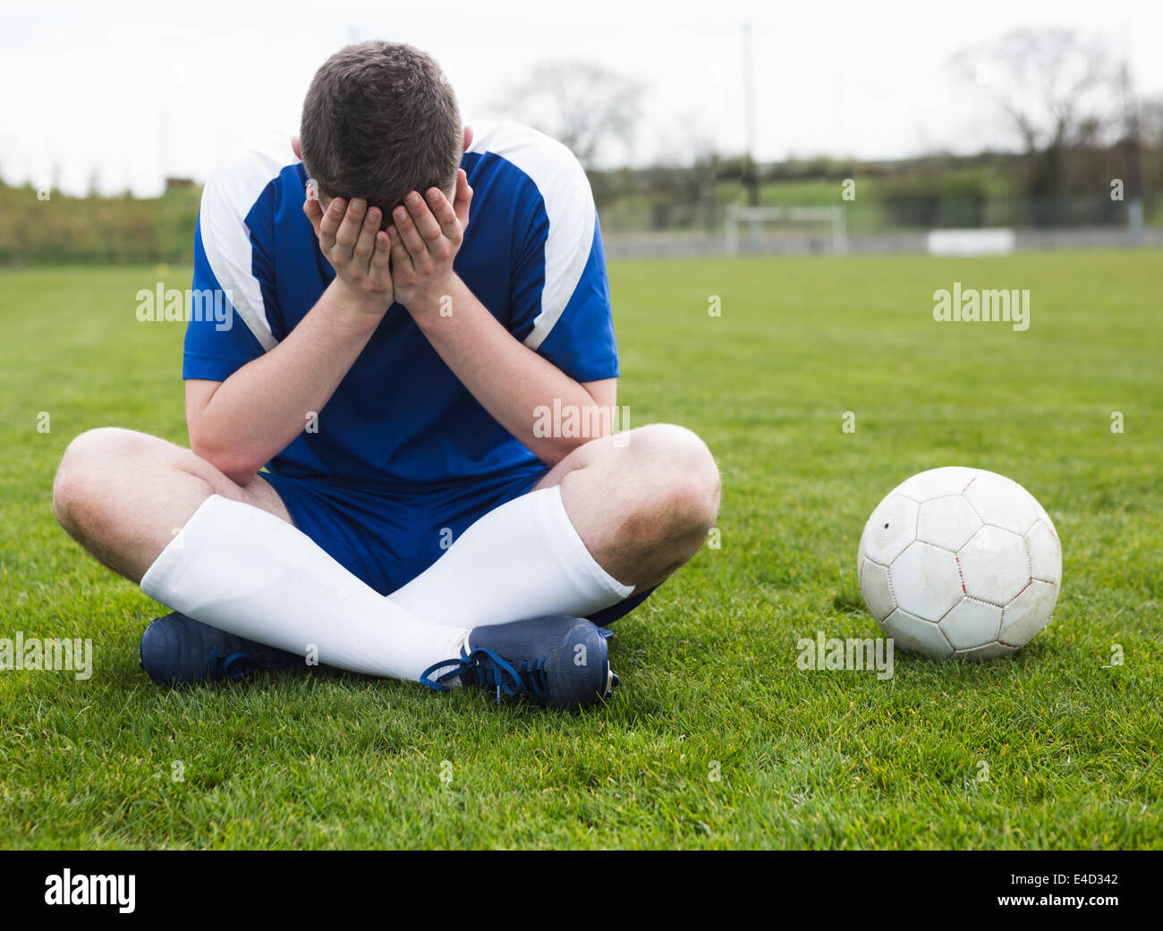 Déçu football player en bleu assis sur pitch après avoir perdu Banque D'Images