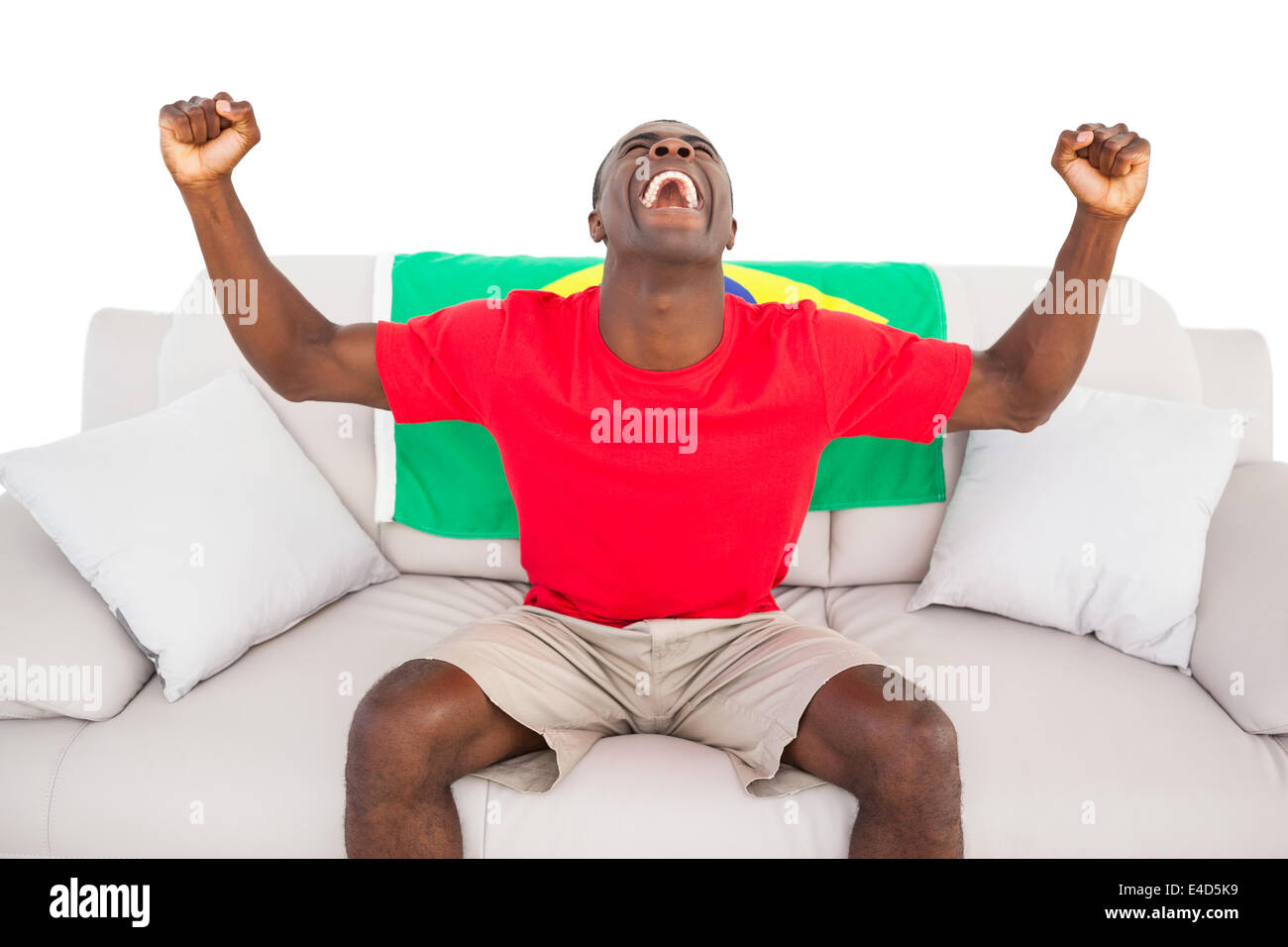 Fan de football brésilien extatique sitting on couch cheering Banque D'Images