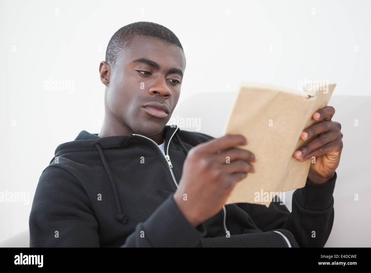 Homme assis sur son canapé en lisant un livre Banque D'Images