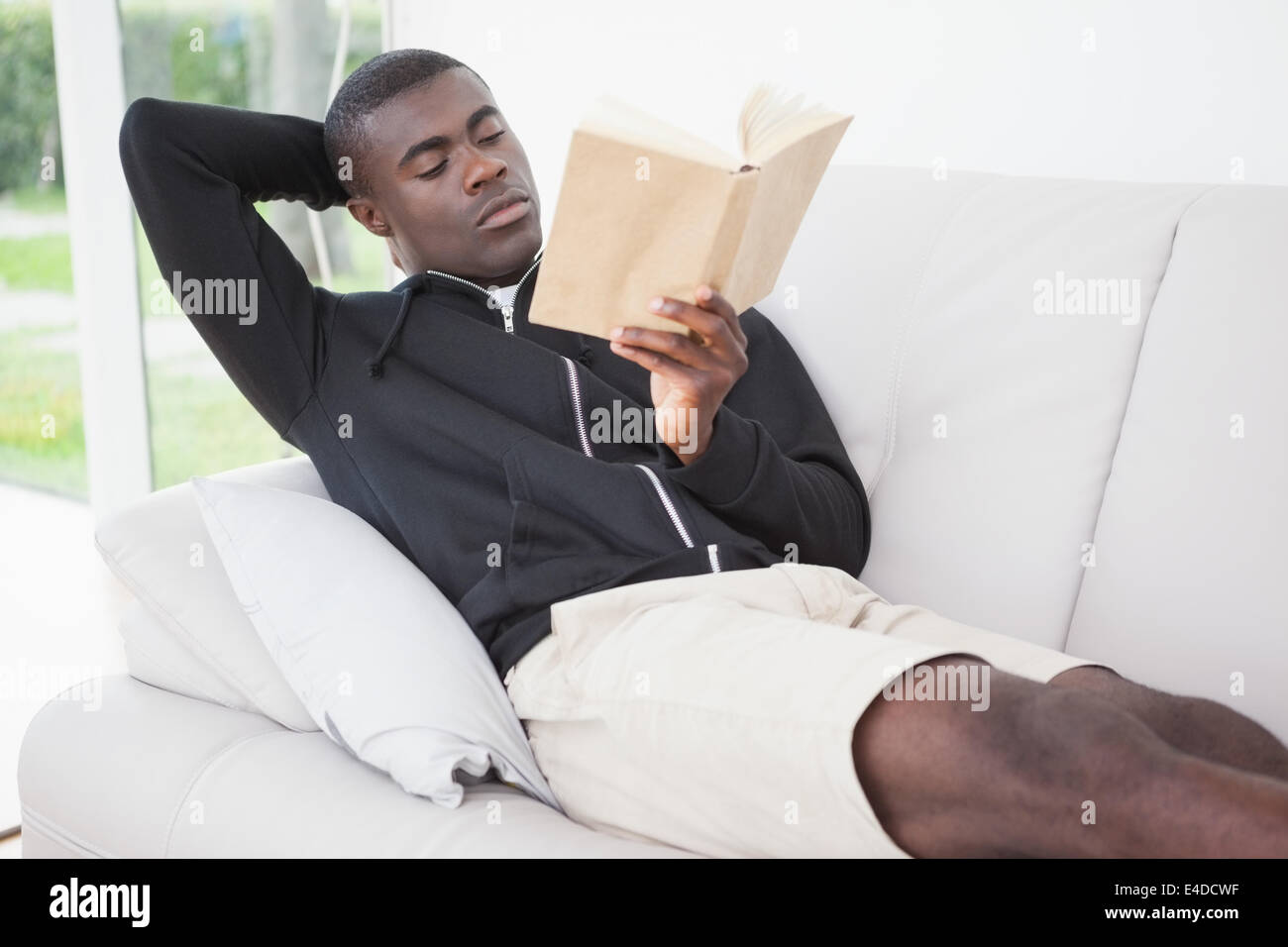 Homme assis sur son canapé en lisant un livre Banque D'Images