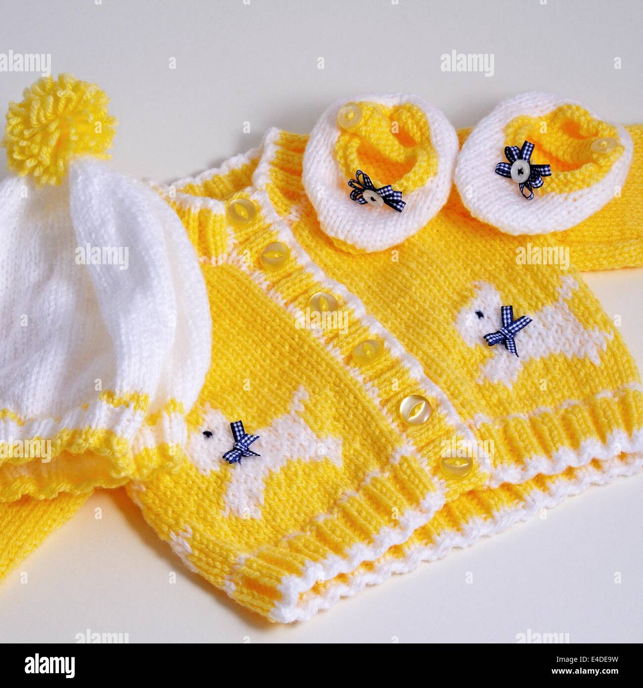 Cardigan jaune tricoté Babys avec Scotty blanc chien avec chapeau et chaussures contre un arrière-plan. Banque D'Images