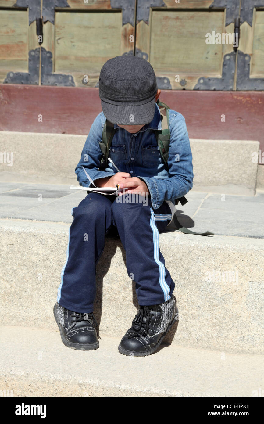 C'est une photo d'un jeune enfant ou d'enfant qui s'asseoir sur un banc en pierre et d'écrire sur un livre. Il est très concentré Banque D'Images