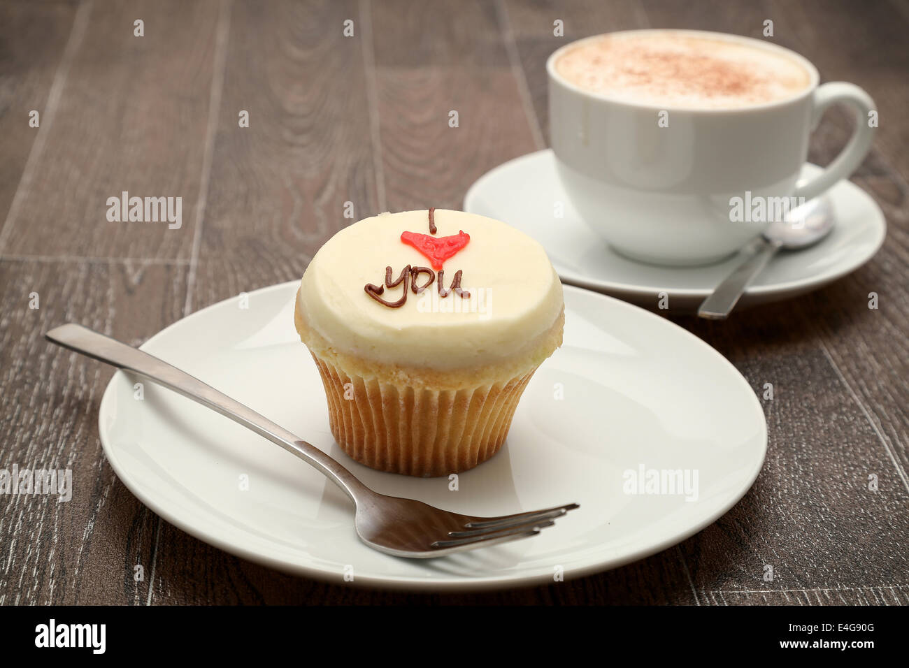 Un petit gâteau recouvert de glaçage buttercream avec le message "I love you" , servi avec un cappuccino, studio shot Banque D'Images