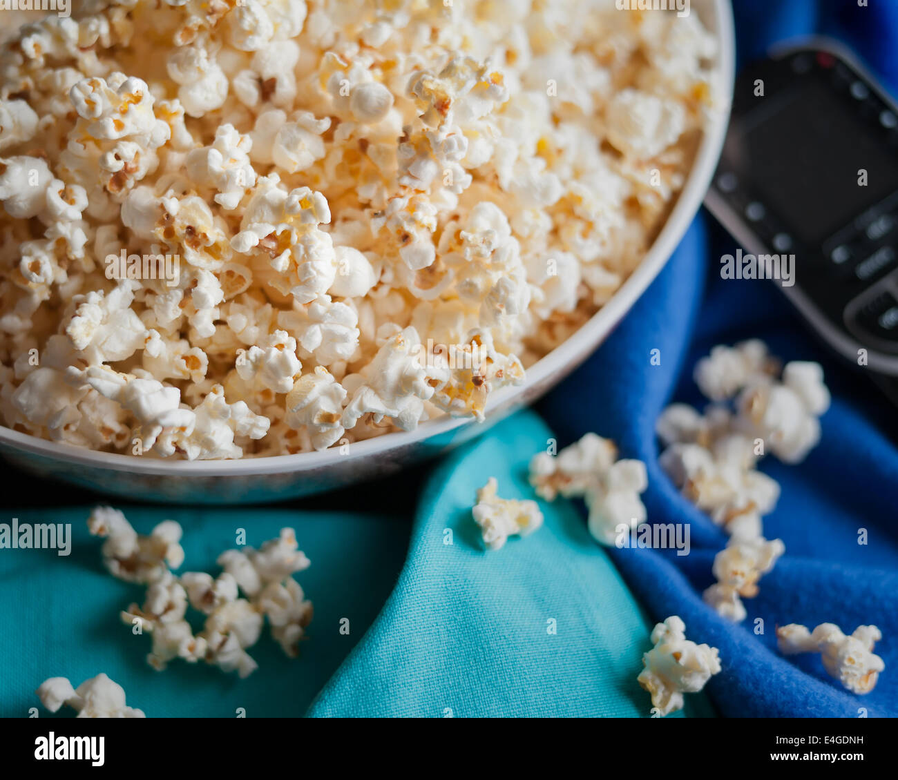 Soirée cinéma avec télécommande, popcorn bol et couverture bleue. Banque D'Images