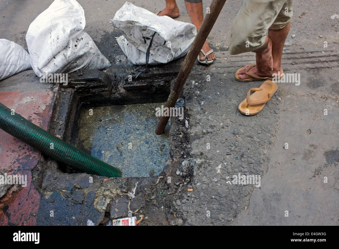 Les hommes sont le pompage d'égout d'un récipient de gouttière sur une rue de ville de Phnom Penh, Cambodge. Banque D'Images