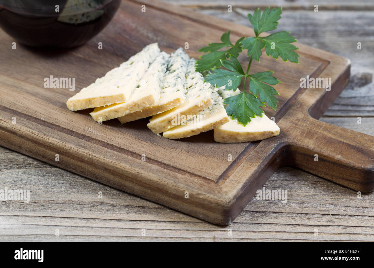 Photo horizontale gros plan de tranches de fromage bleu, le persil sur le côté, sur un serveur traditionnel en bois avec un verre de vin rouge partielle Banque D'Images