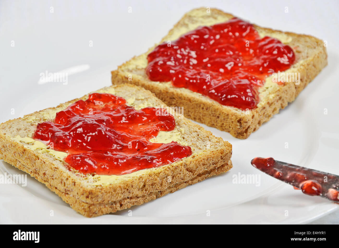 Deux tranches de pain grillé avec de la confiture de fraise et beurre sur plaque blanche avec couteau, Close up, Banque D'Images