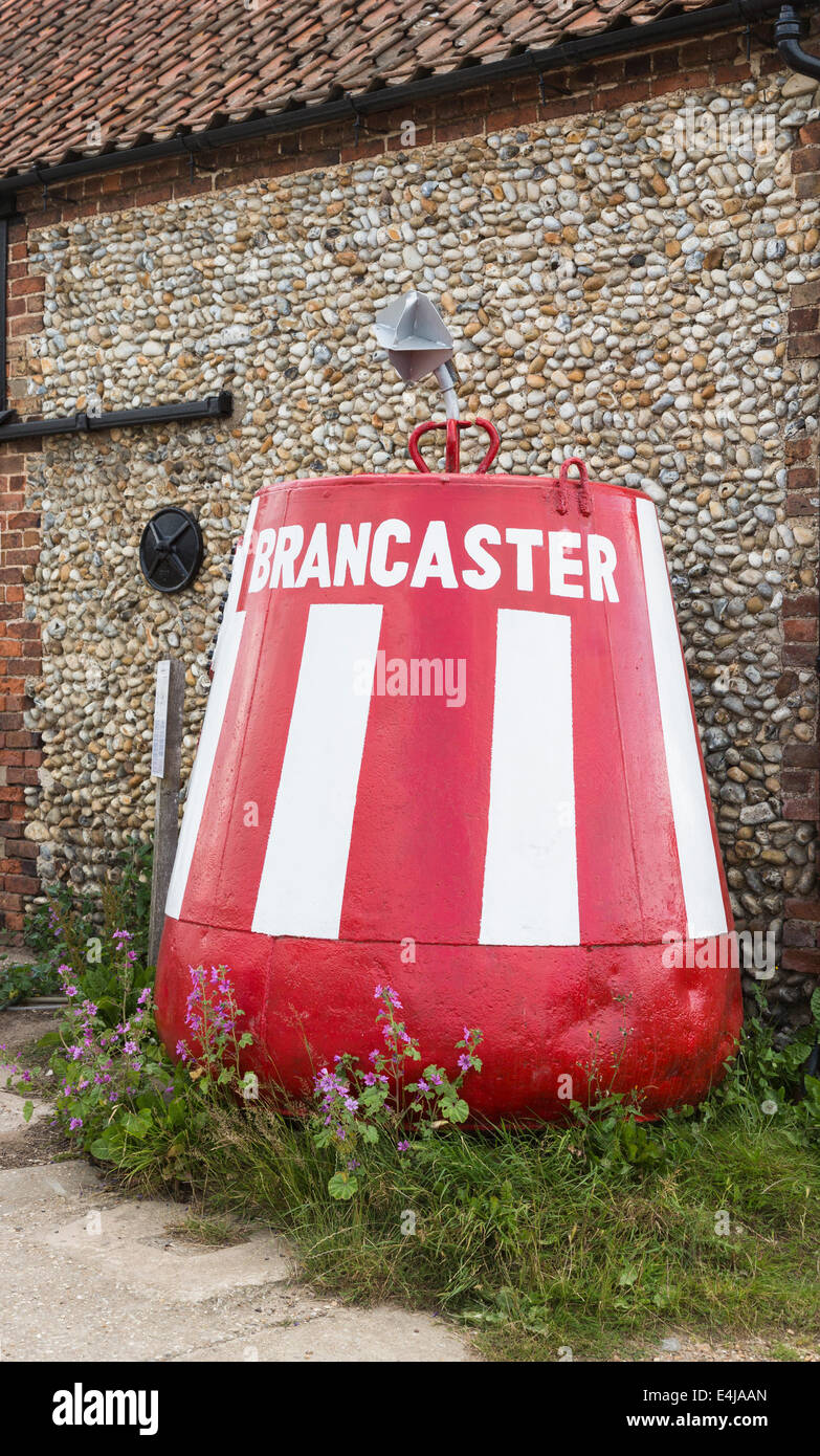 Bouée rouge et blanc à rayures peintes avec le nom 'Brancaster', un petit village côtier de North Norwich Banque D'Images