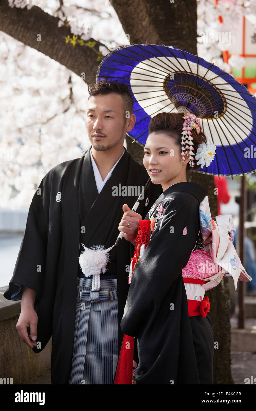 Jeune couple en tenue de mariage traditionnelles posent au milieu des cerisiers en fleurs dans le quartier Higashi Chaya de Kanazawa Banque D'Images