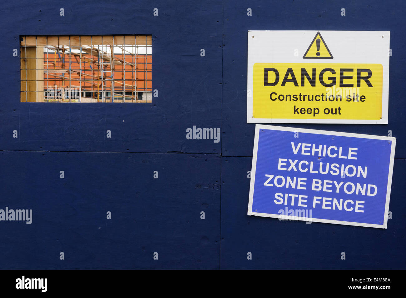Clôture autour d'un site de construction, avec une fenêtre découpée permettant aux gens de voir à travers, et des panneaux d'avertissement Banque D'Images