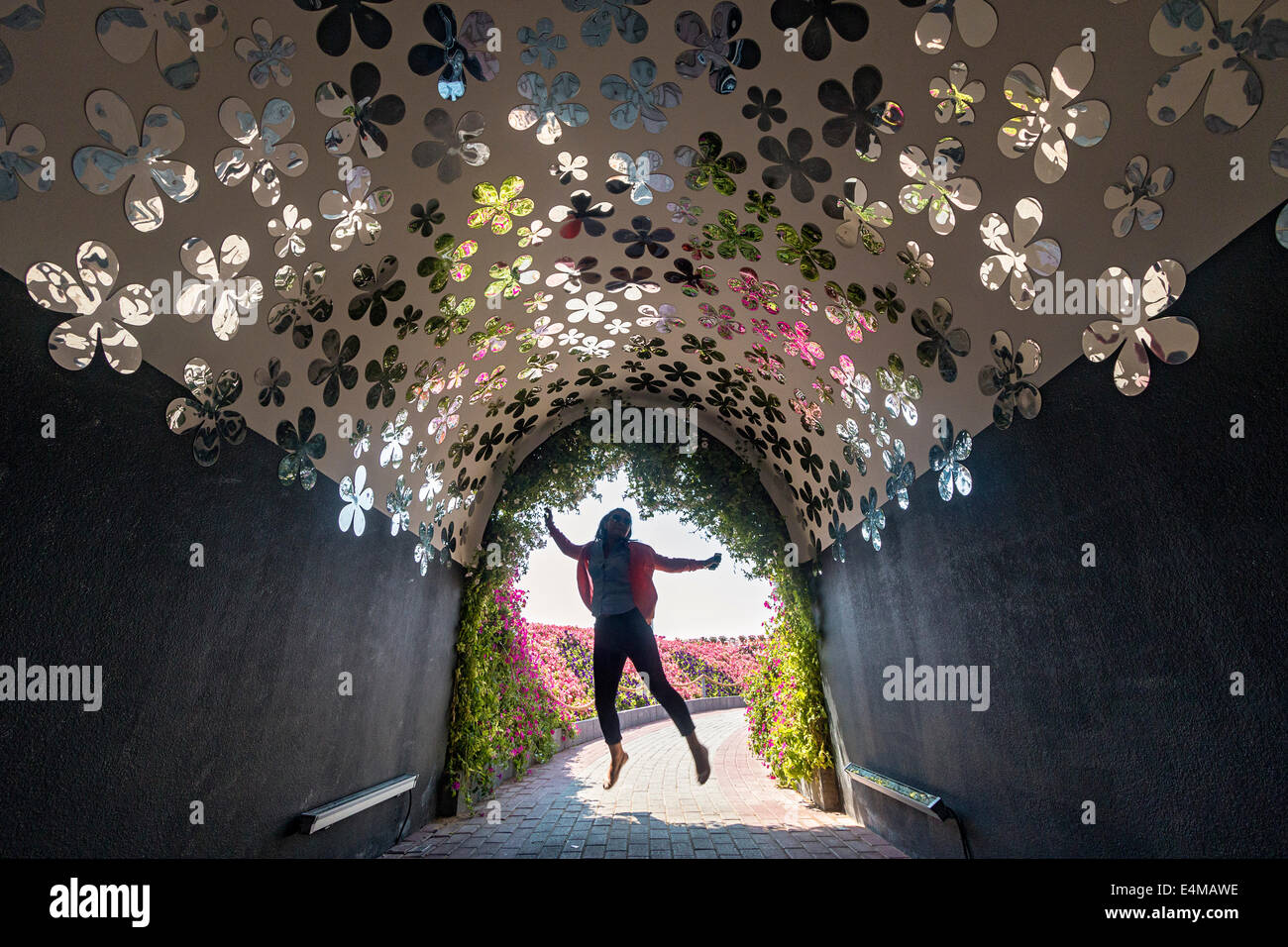 Tunnel de réflexion 'fleurs' reflètent les vraies fleurs à l'extérieur en tant que visiteur saute de joie à Dubai's Miracle Garden Banque D'Images