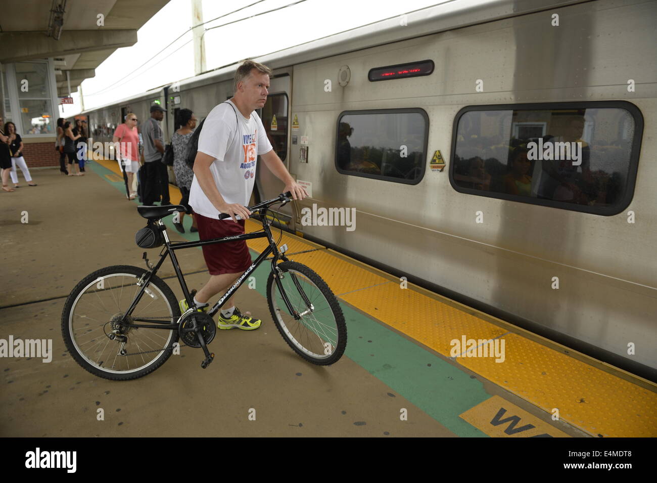 Merrick, New York, États-Unis - 14 juillet 2014 - Pendant l'heure de pointe du soir, un homme se promène avec son vélo sur une plate-forme surélevée à bord des trains à Merrick gare de Babylone, de la direction générale après MTA Metropolitan Transit Authority et Long Island Rail Road Union européenne parle de l'impasse, avec un potentiel d'LIRR imminente grève juste quelques jours auparavant. Credit : Ann E Parry/Alamy Live News Banque D'Images