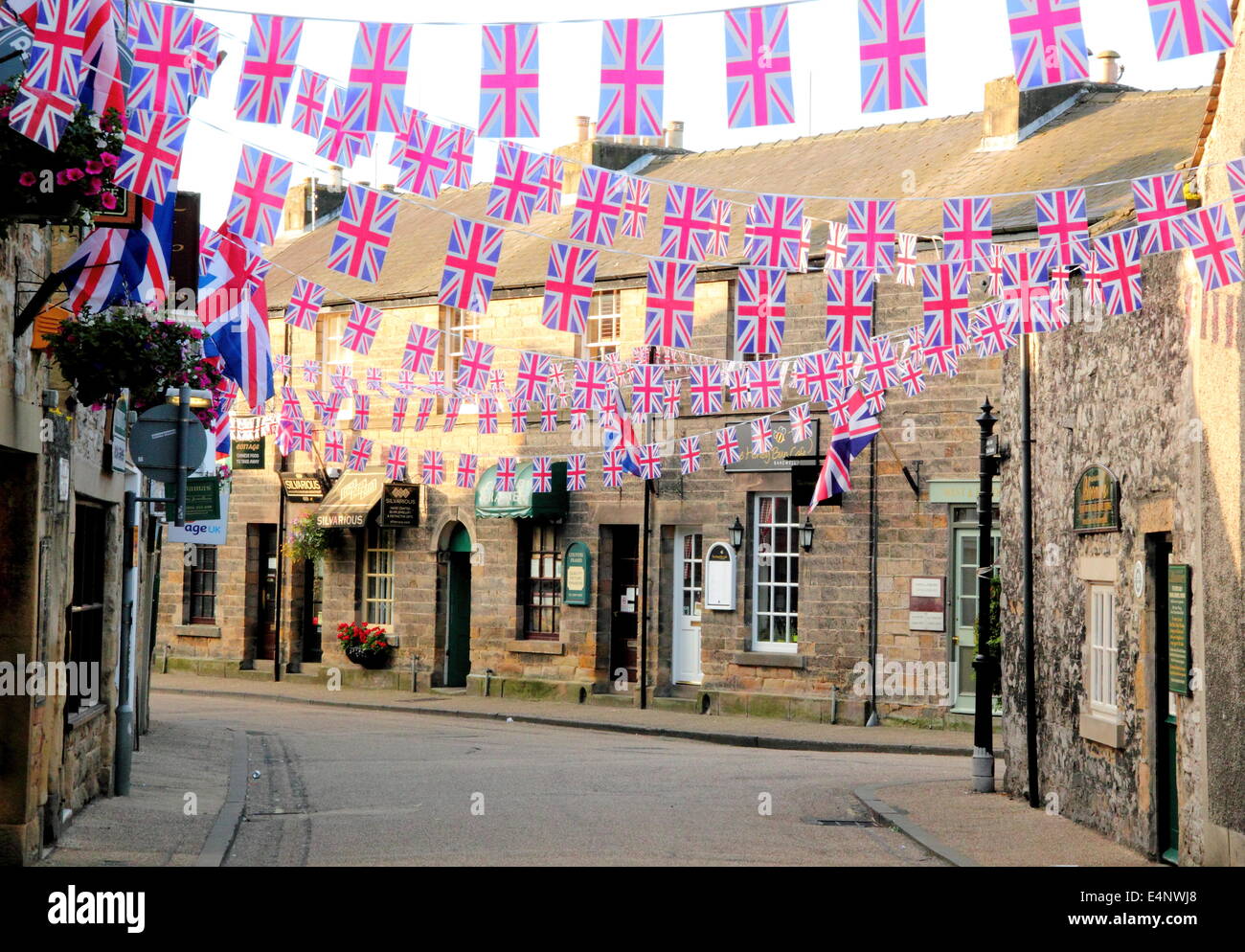 Union Jack noir et volant au-dessus d'une rue commerçante du centre-ville de Bakewell ; une ville historique marché anglais - l'été, UK Banque D'Images